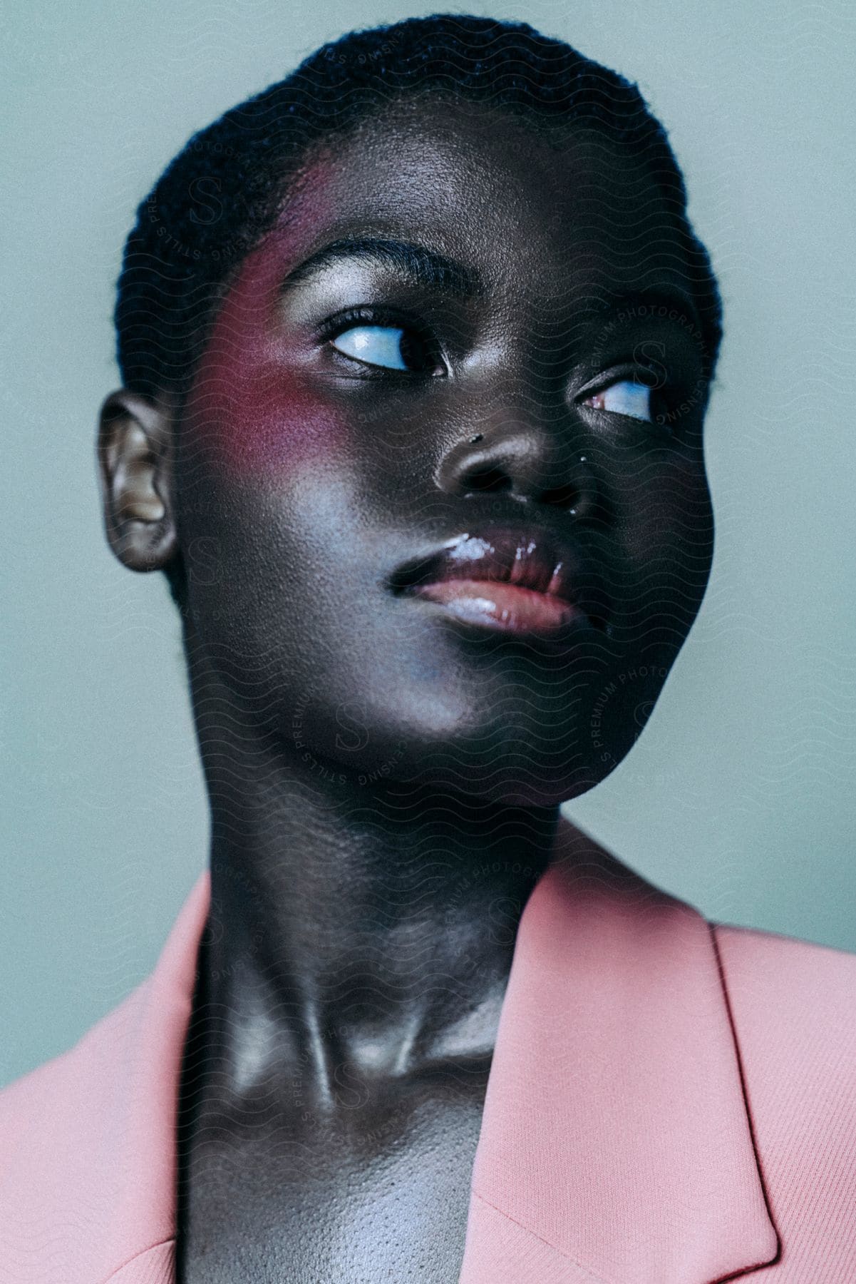 The face of a black woman wearing a pink outfit and pink makeup on her lower forehead and she is looking to the left side