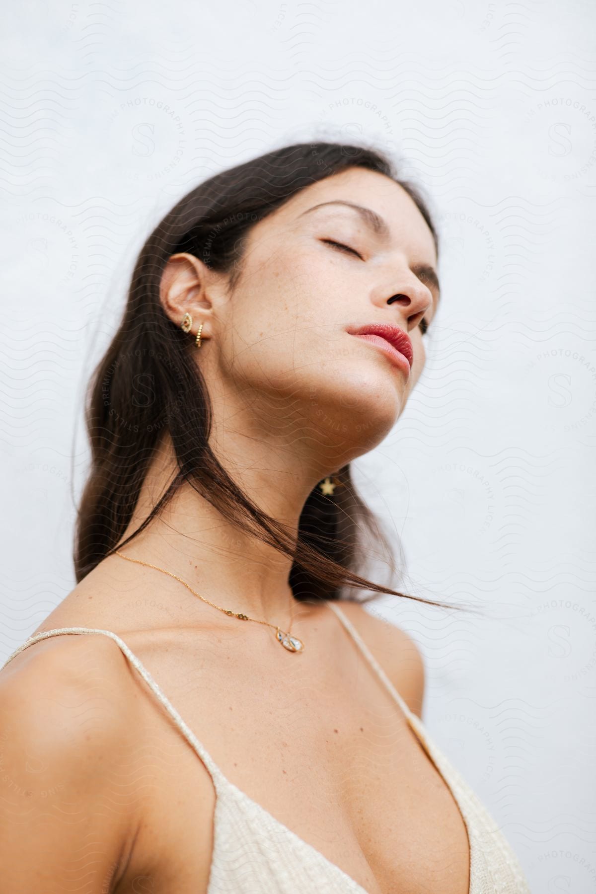 A woman stands with her head tilted and eyes closed