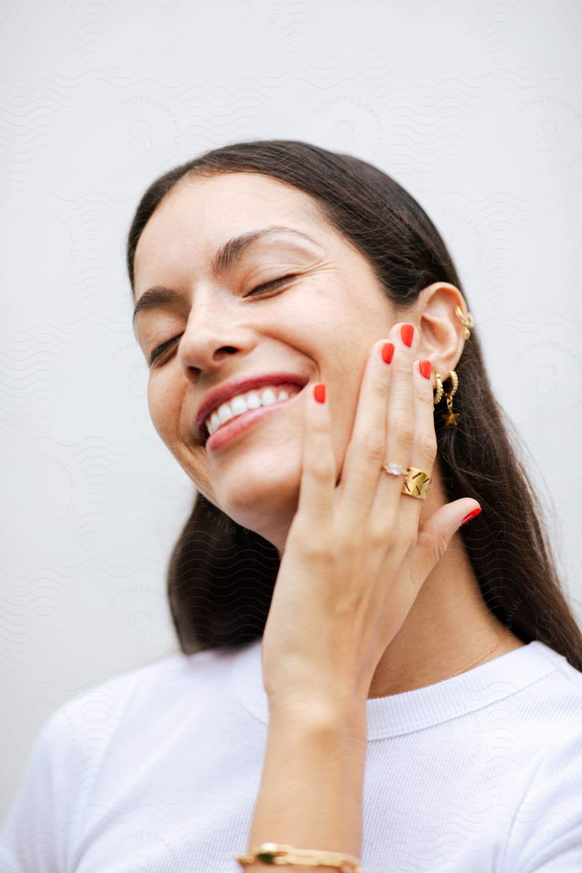 A woman smiling wide while she models rings on her fingers and earrings