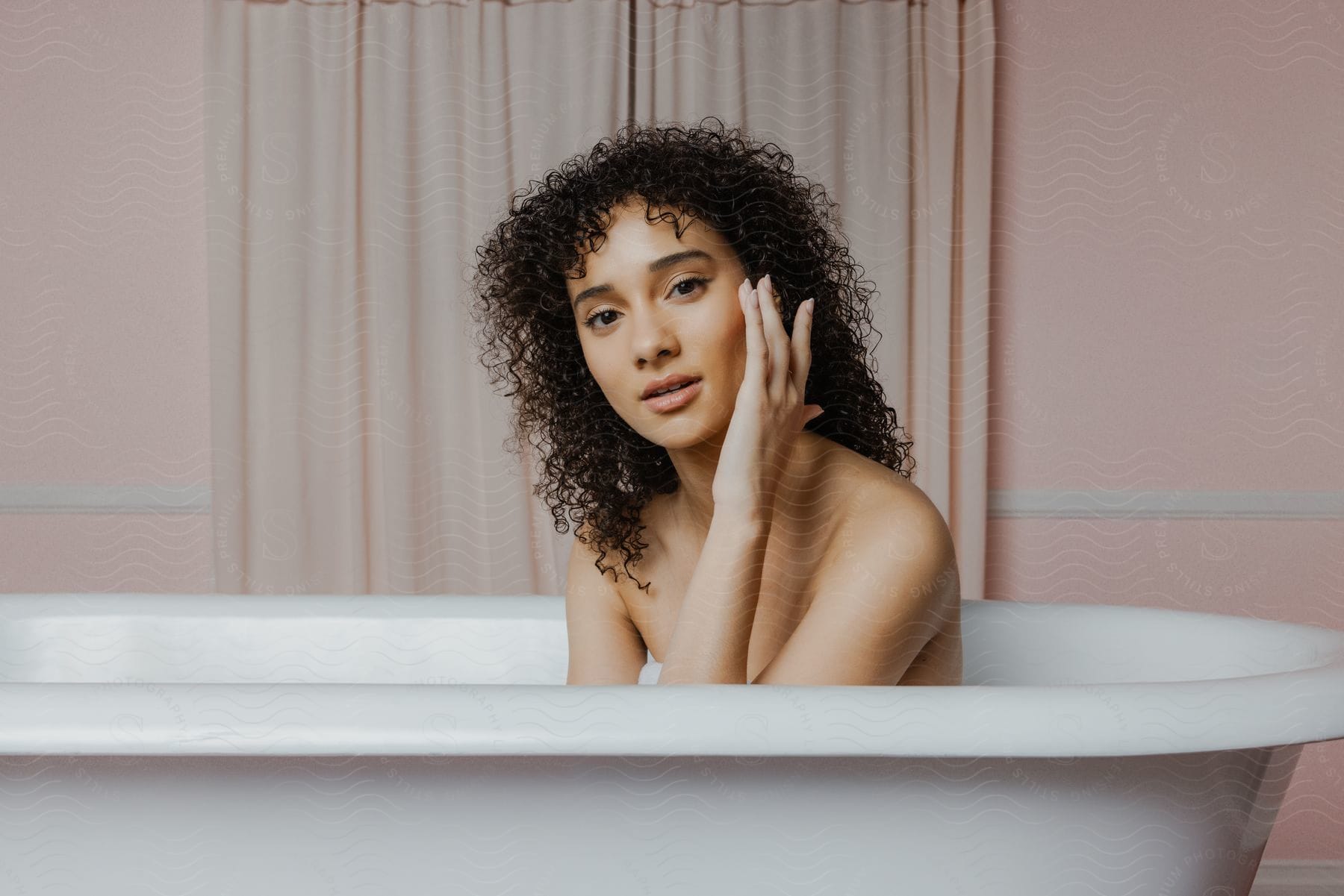 A woman is sitting in a bathtub holding her face using her hand and is looking straight ahead