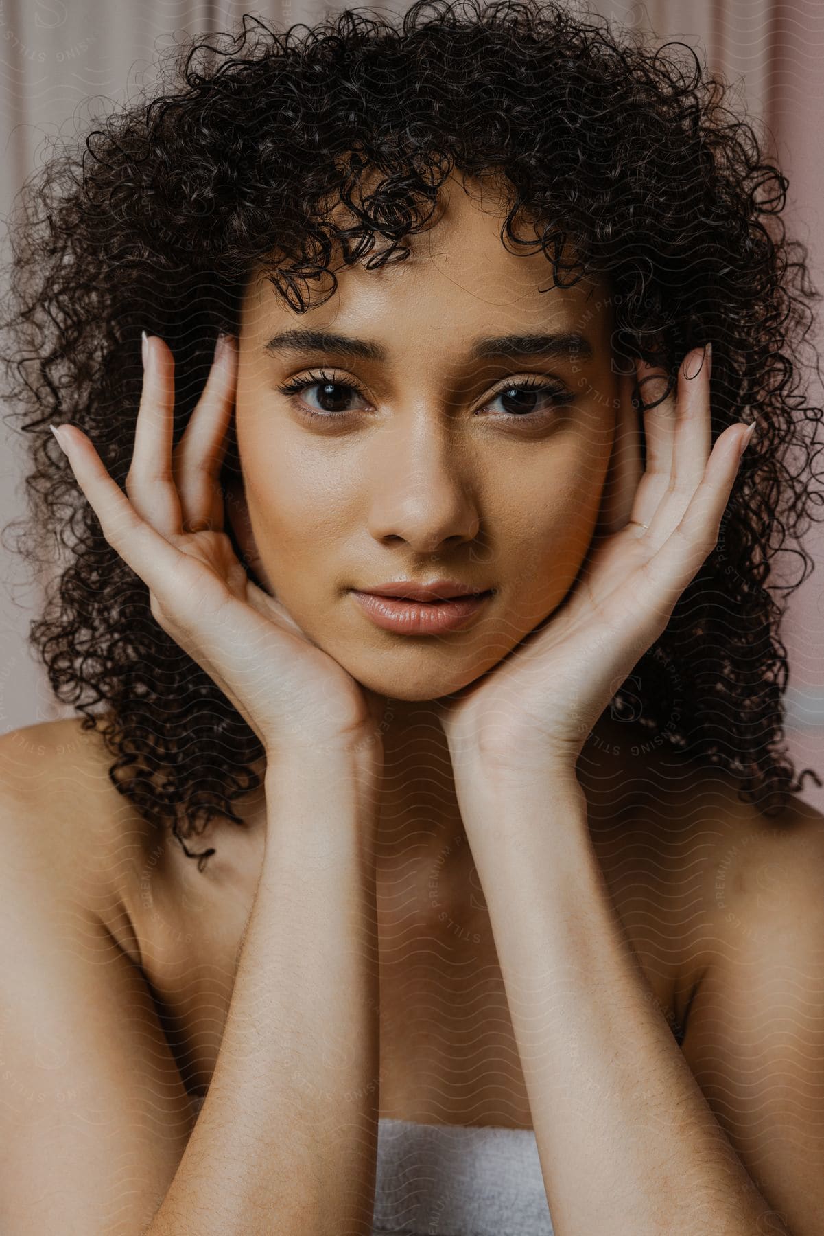 Close-up of a young woman wearing a bath towel while holding her hands on the sides of her face.