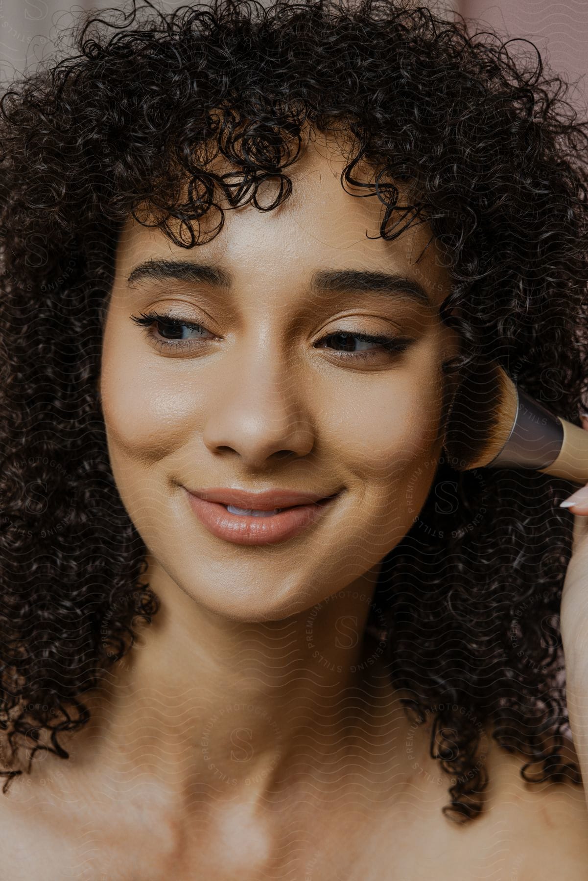 Portrait of a young curly-haired woman applying blush to her face