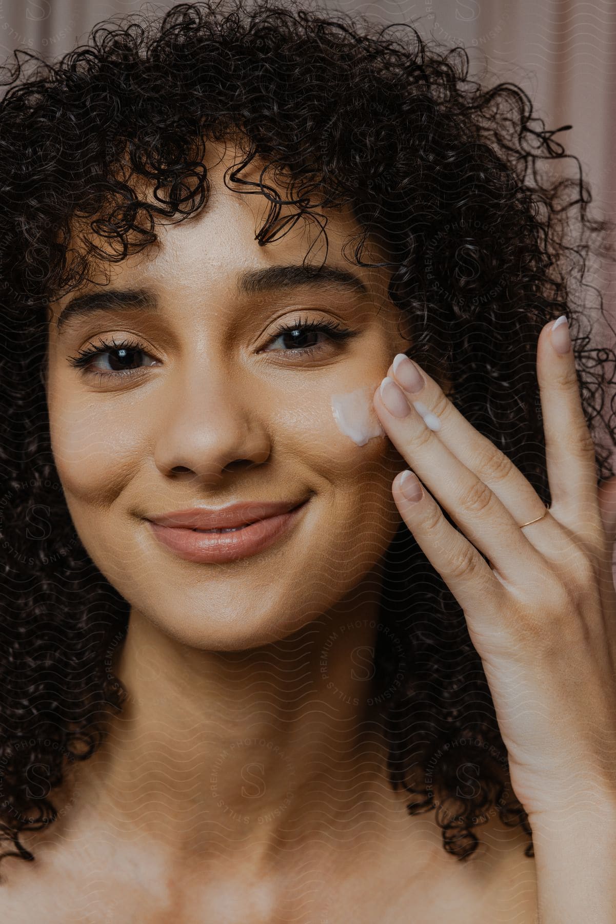 Portrait of a young woman with curly hair applying cream to her face