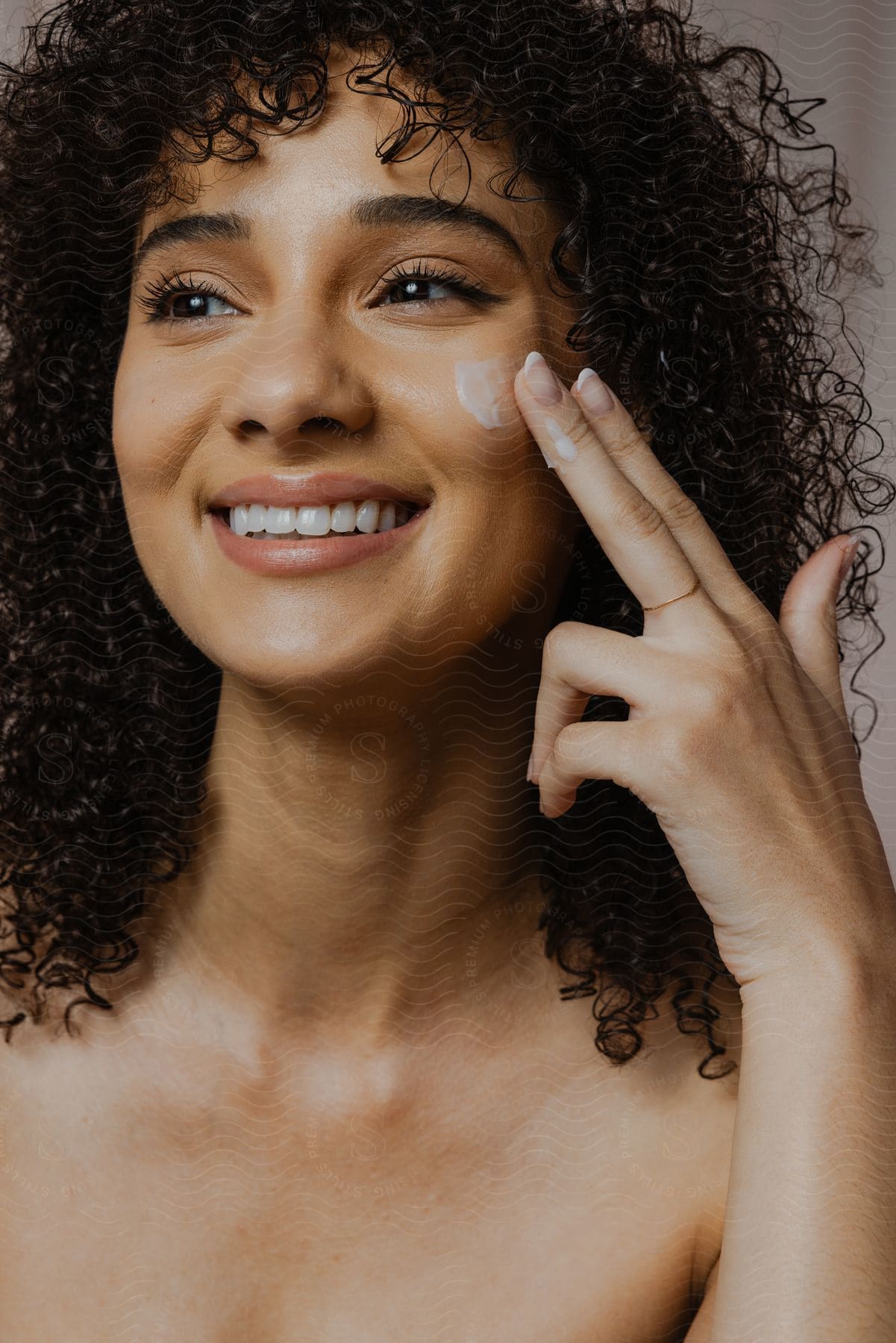 A woman smiles as she puts cream on her cheek with her fingers