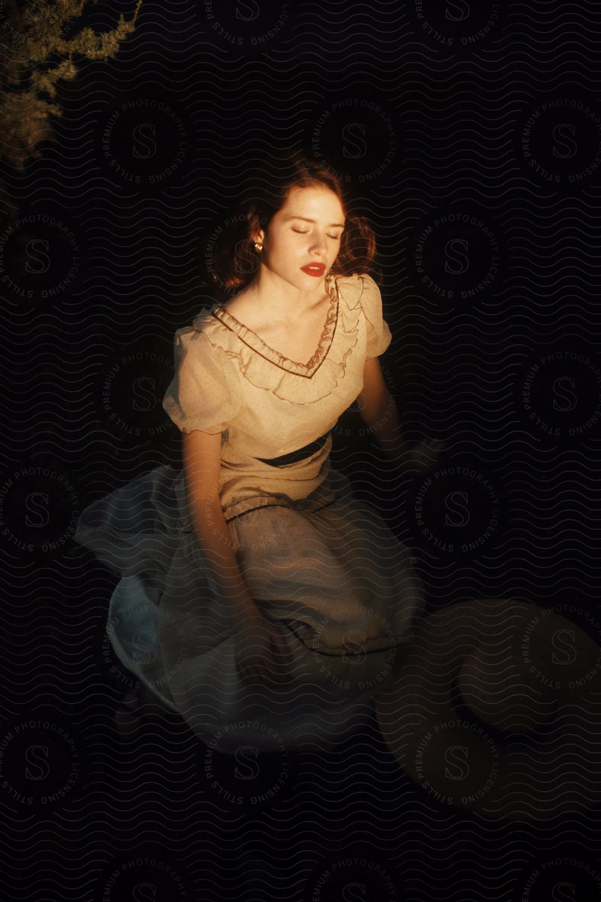 A young woman sits and models a white dress outdoors at night.