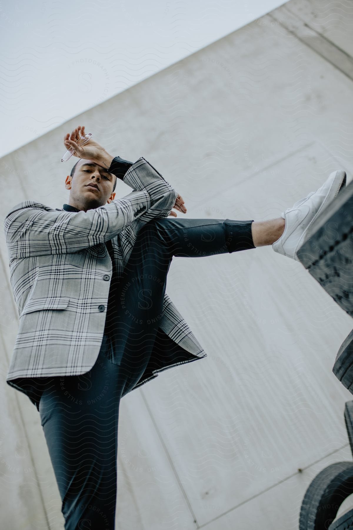 A young man in a stylish plaid blazer and trousers striking an artistic pose.