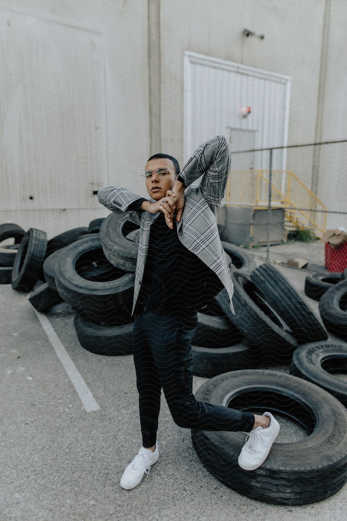 A man posing in a parking lot with tires lying on the ground.