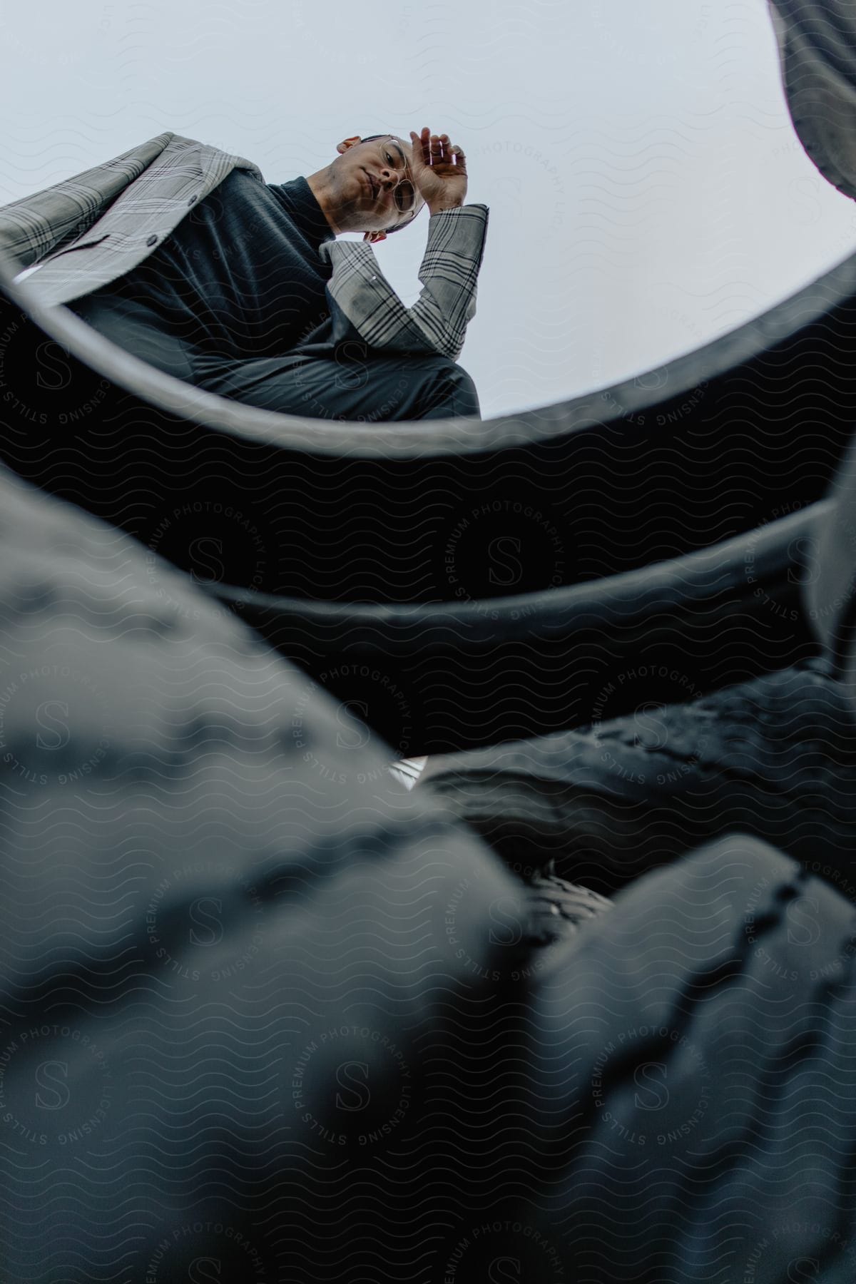 Model man in blazer under tires in an open place on a cloudy day.