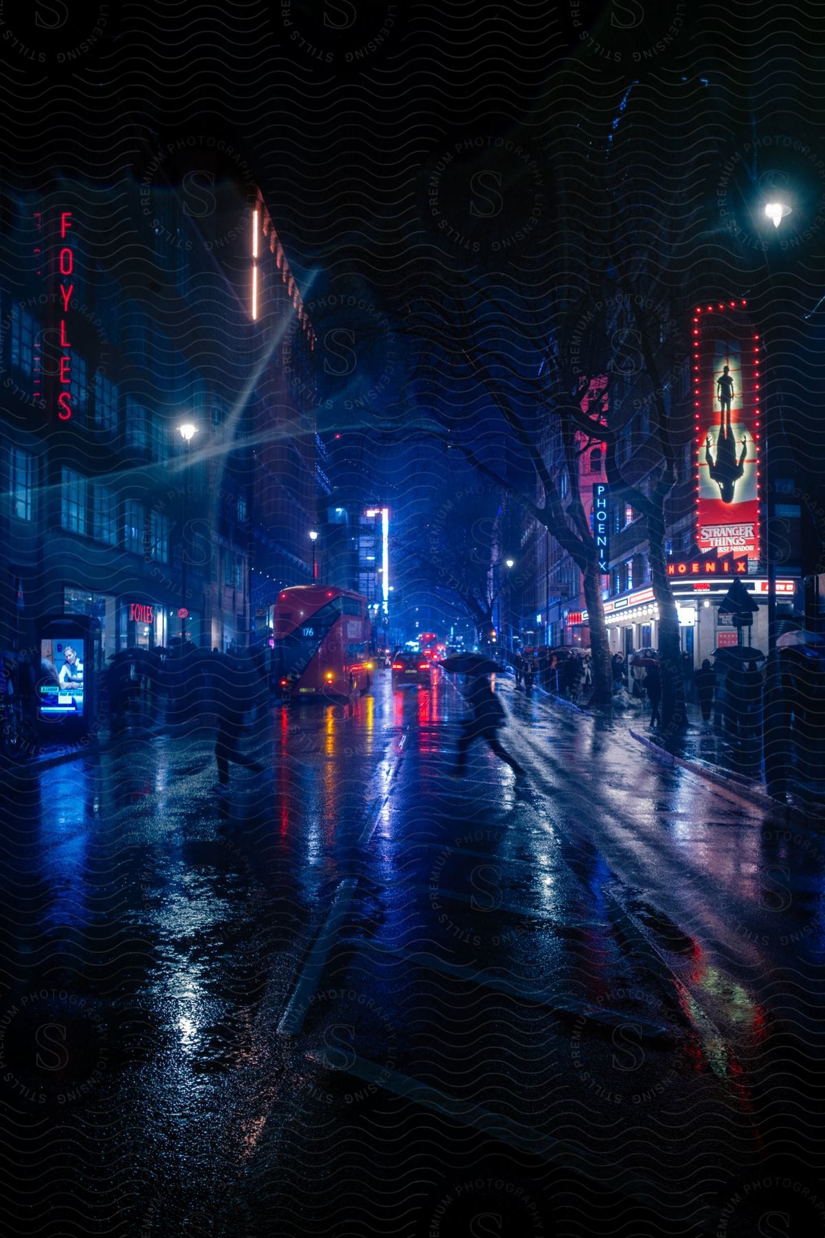 Lights on downtown buildings and automobiles glow in the darkness as people cross a rainy street