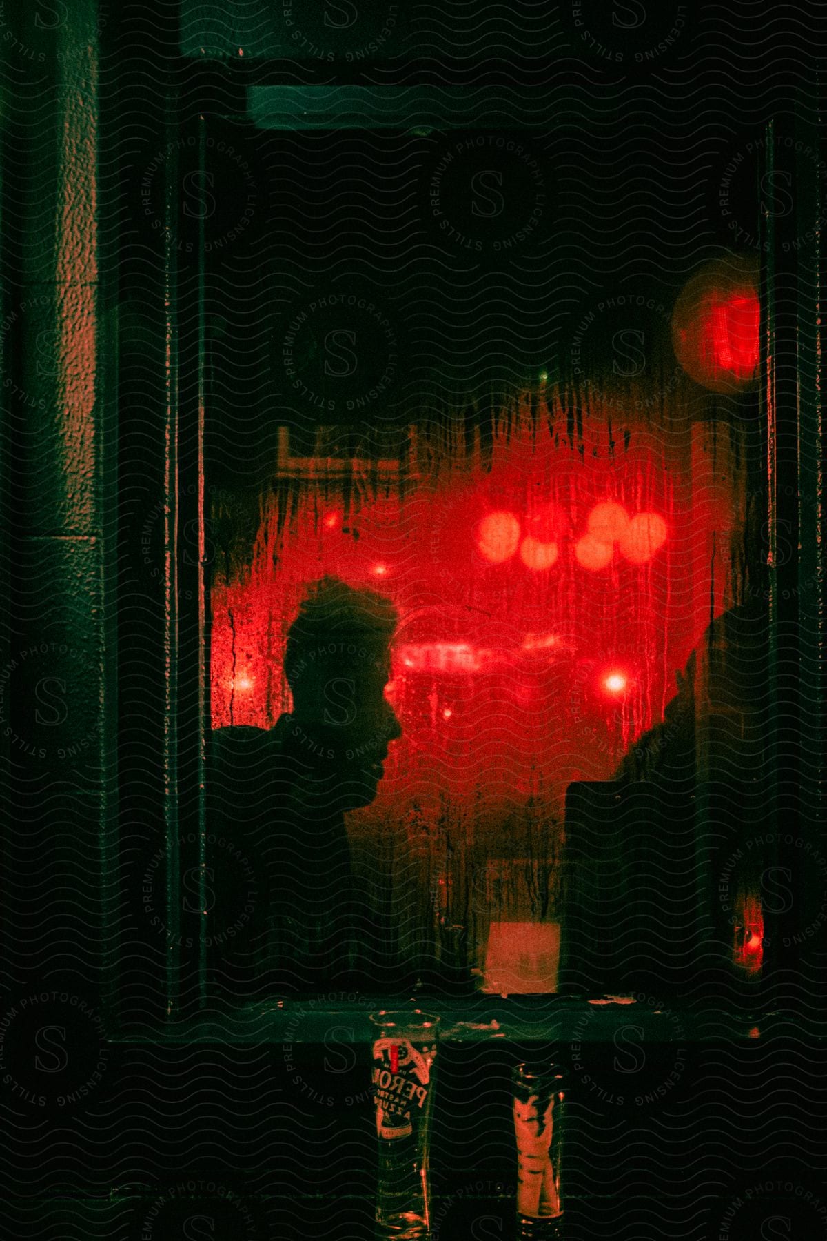 Window of a sweaty bar with the silhouette of a person and with red lights and radiating two glasses of beer with foam at night