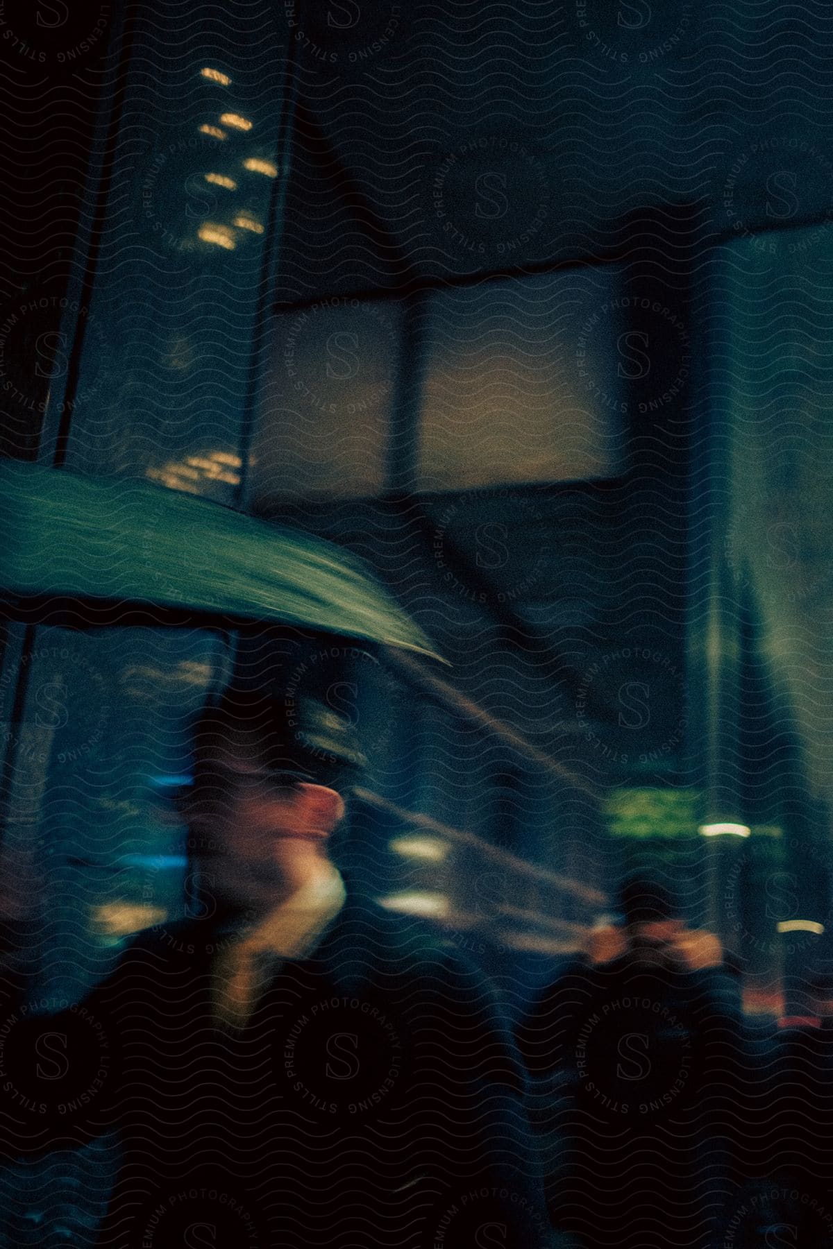 Stock photo of a person with a green umbrella walks through a rainy night city, his face obscured.