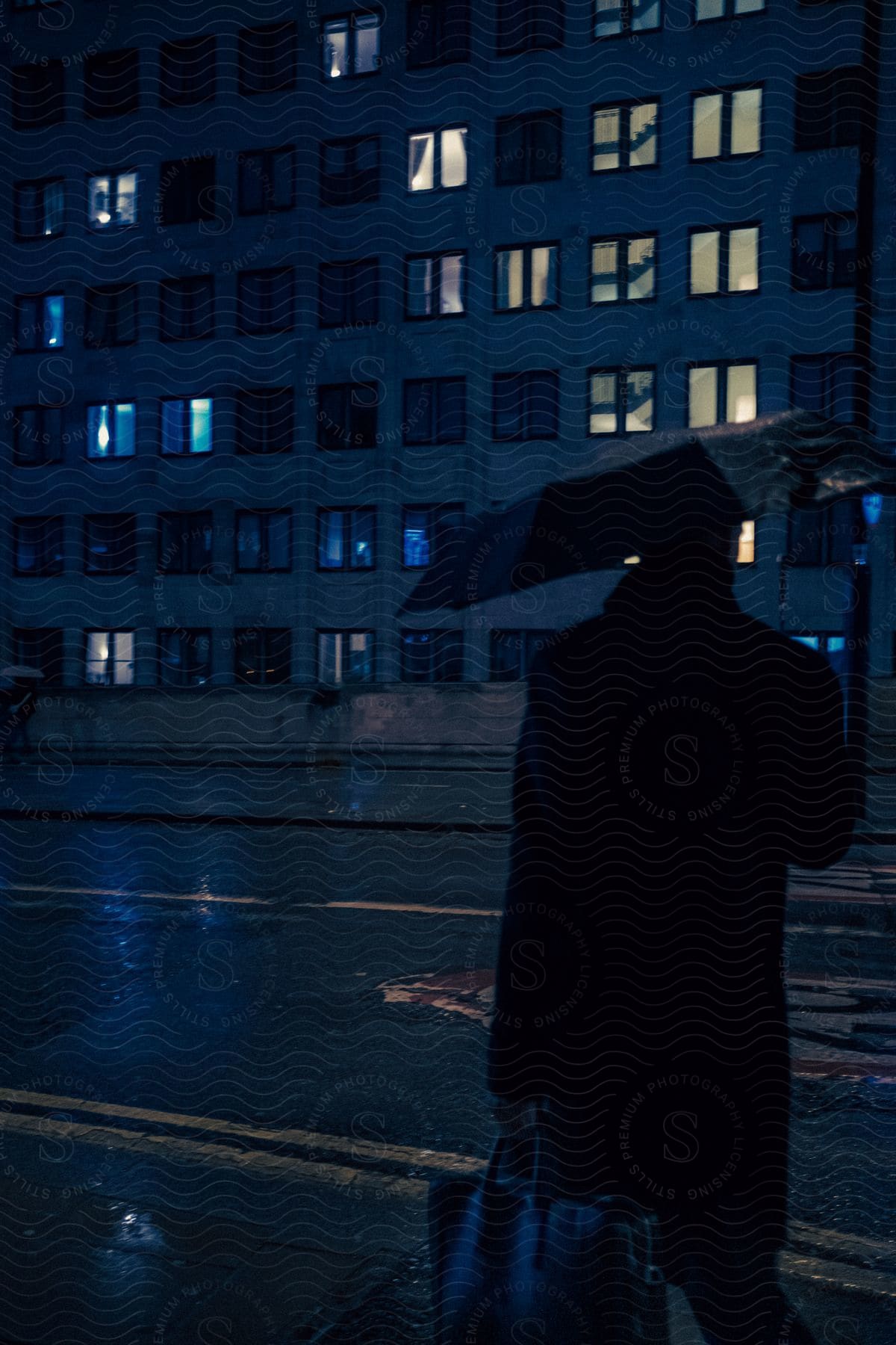 A man walks on a rainy downtown street holding up his umbrella and carrying his bag