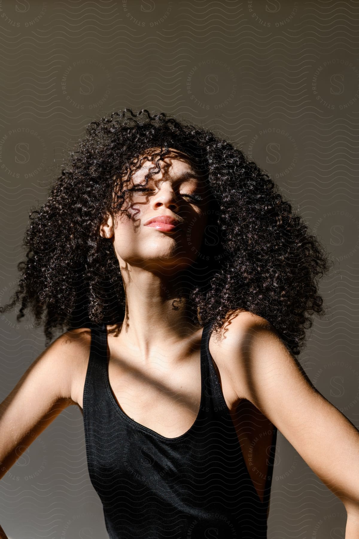 Face of a young woman with curly hair wearing a black tank top and the sun's reflection under her face.