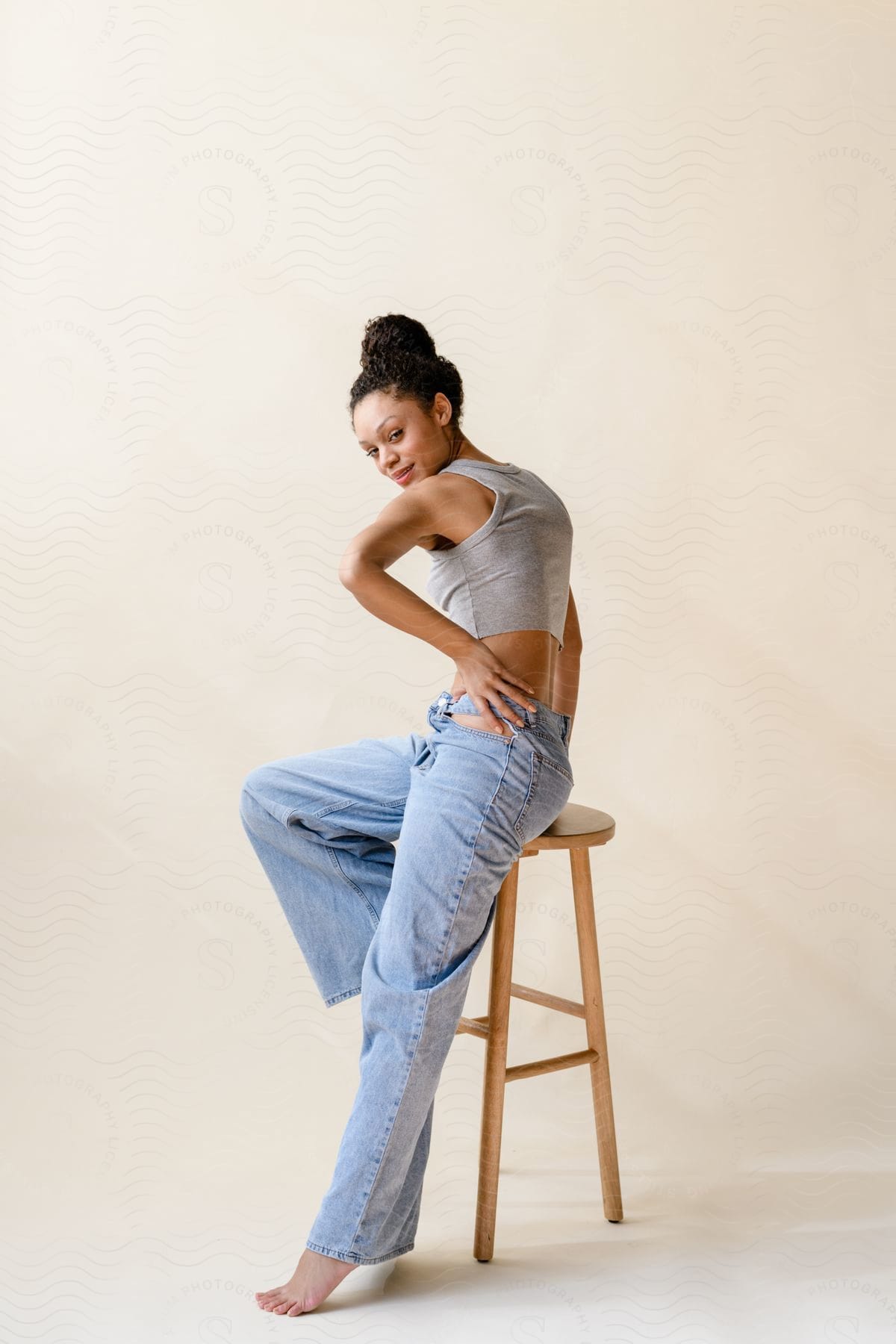 Model sitting on a wooden bench wearing jeans and a gray t-shirt inside a studio with a white background