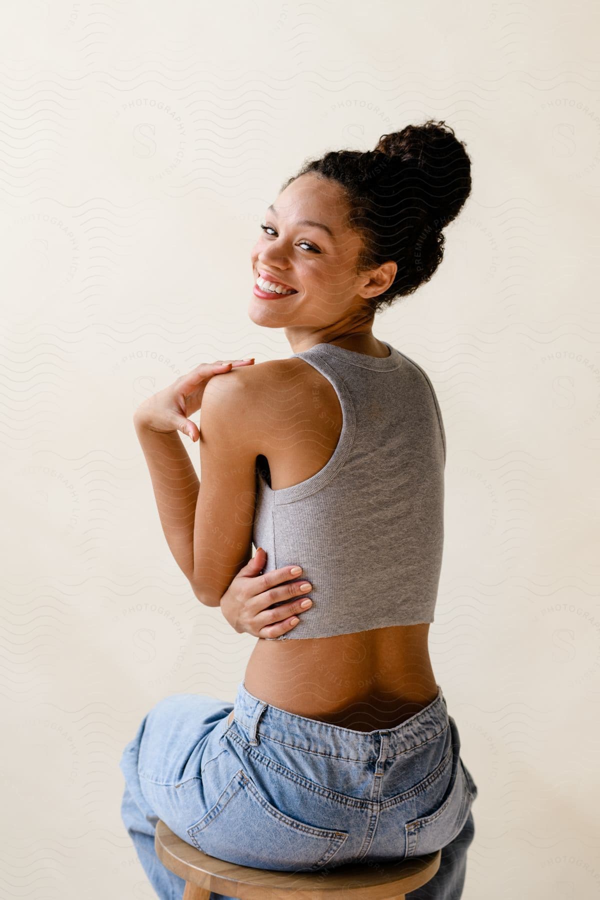 Woman sitting on a stool turns around and smiles with her hands on her shoulder and side