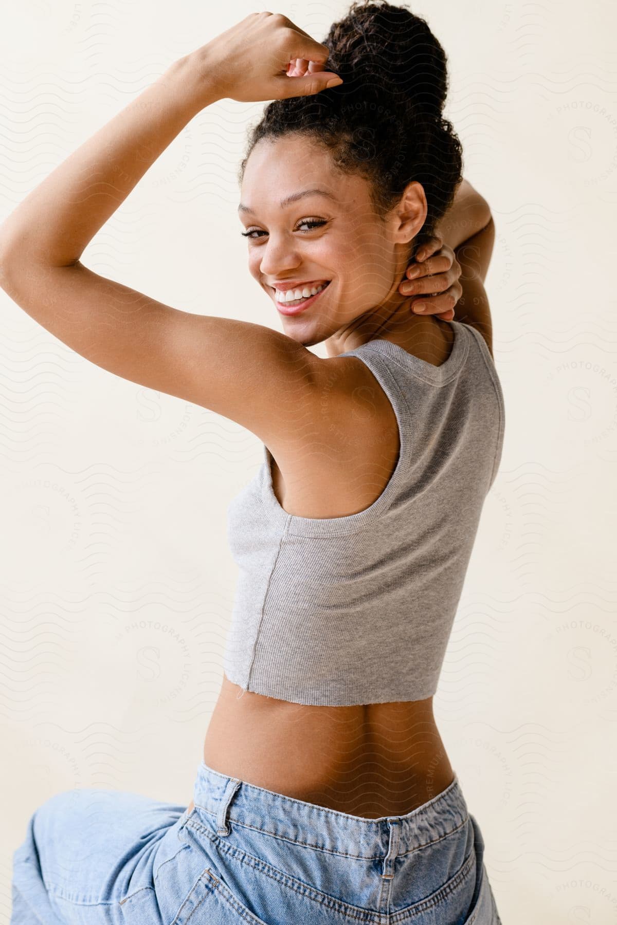 Young model posing with hands on head and wearing a gray shirt and jeans.