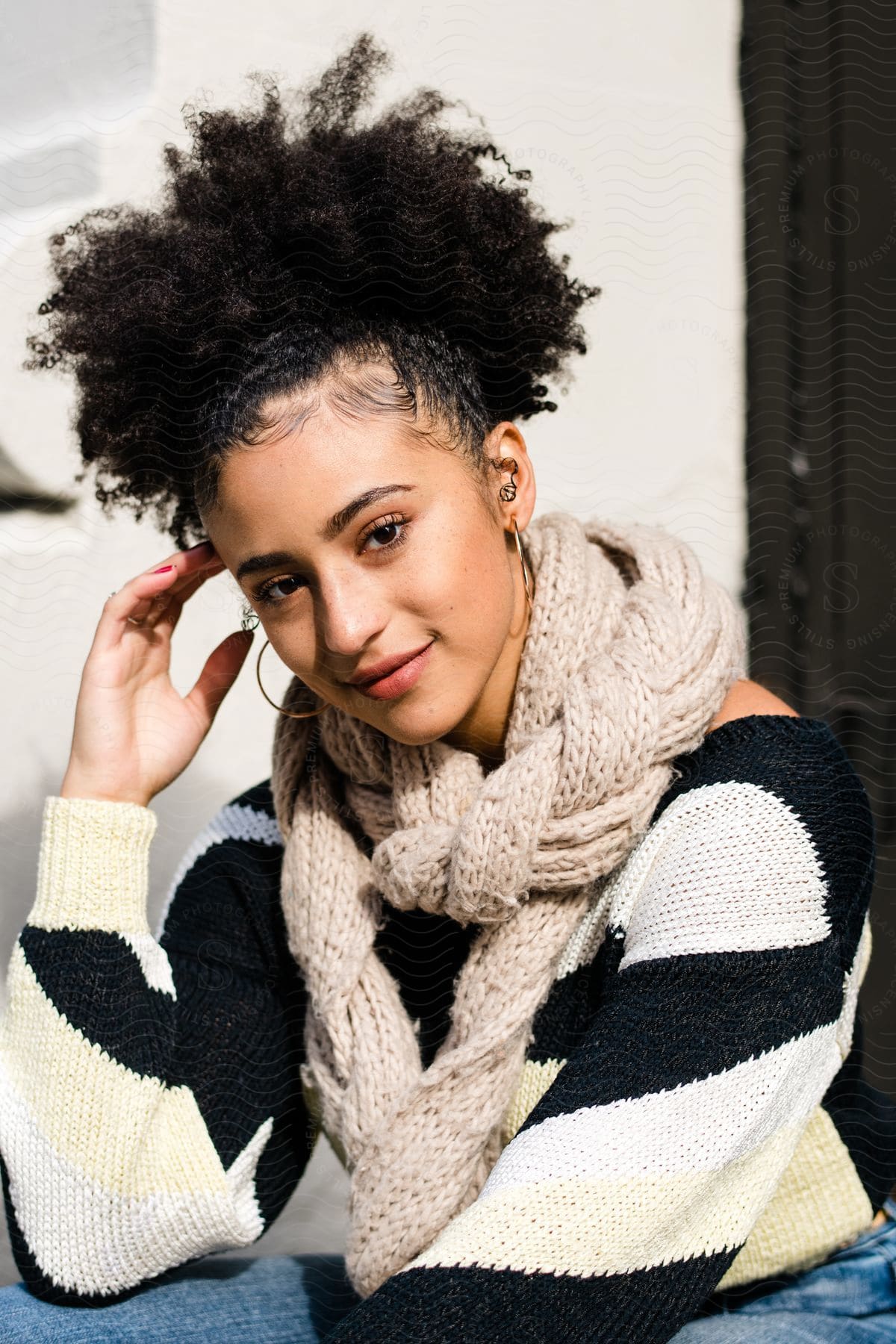 Young model with afro curly hair wearing one hand on her forehead and wearing a gray scarf