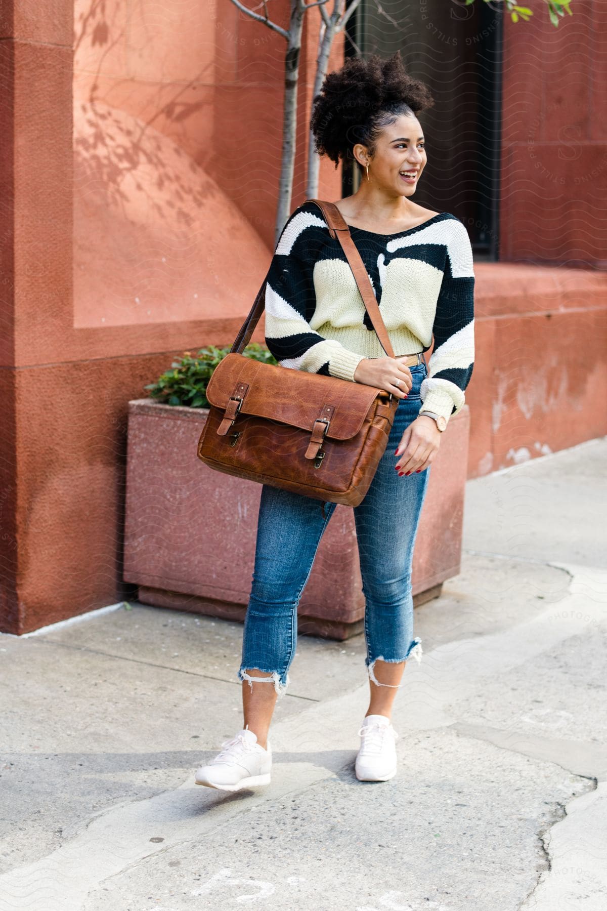 a young female holding a leather handbag wearing jean and sweat pant walking on the side walk