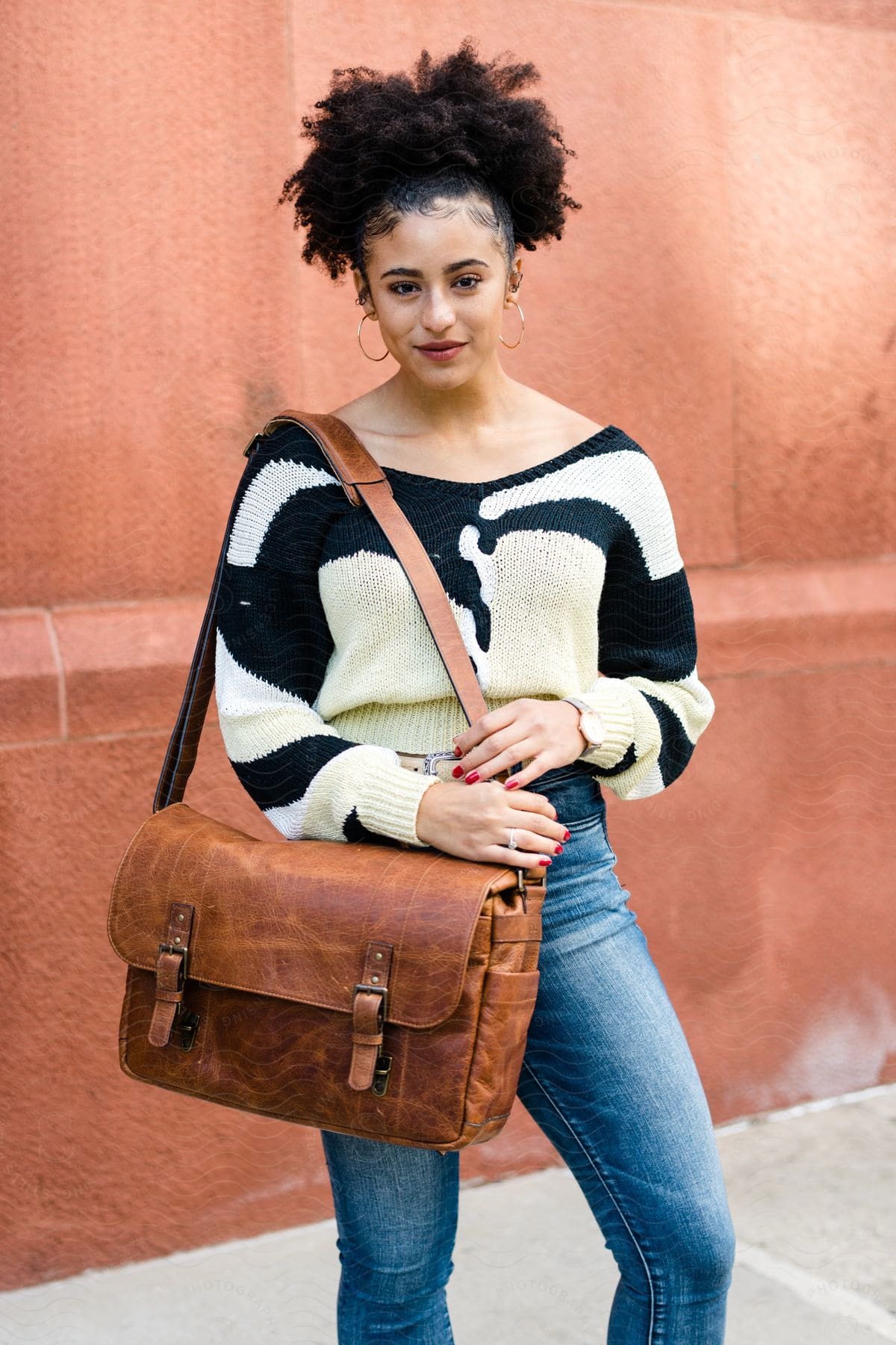 Young woman modeling with a leather shoulder bag, jeans and a blouse in an outdoor environment