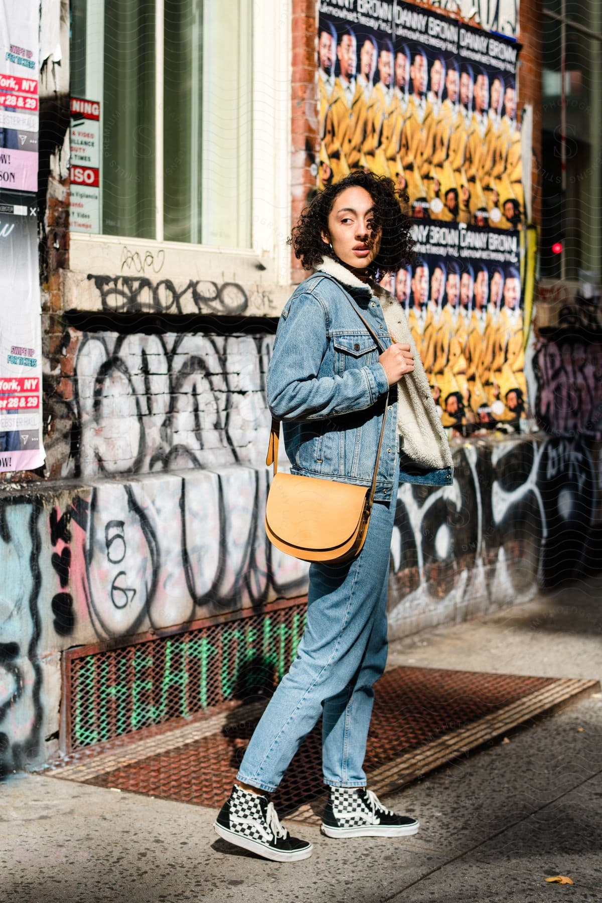 Woman modeling an all-denim look with a crossbody bag next to graffiti-covered walls around the city