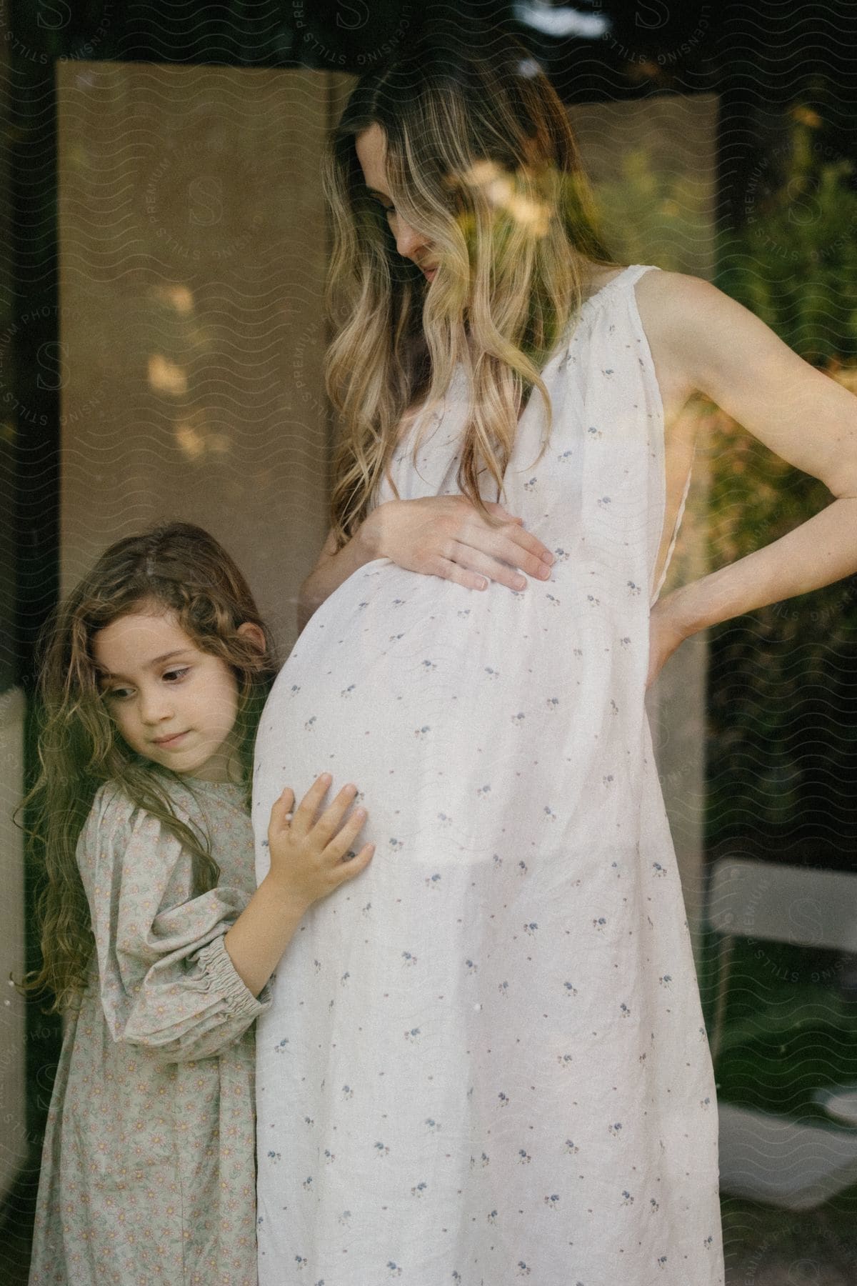 A young girl is hugging and resting her head on the belly of a pregnant woman.