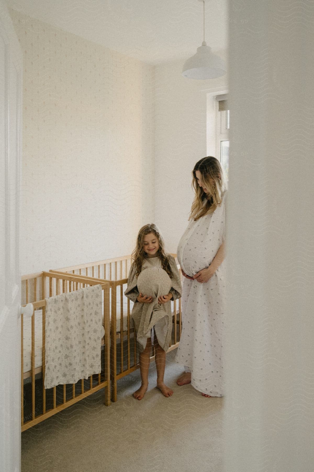 A pregnant mother standing around with her daughter in a room.