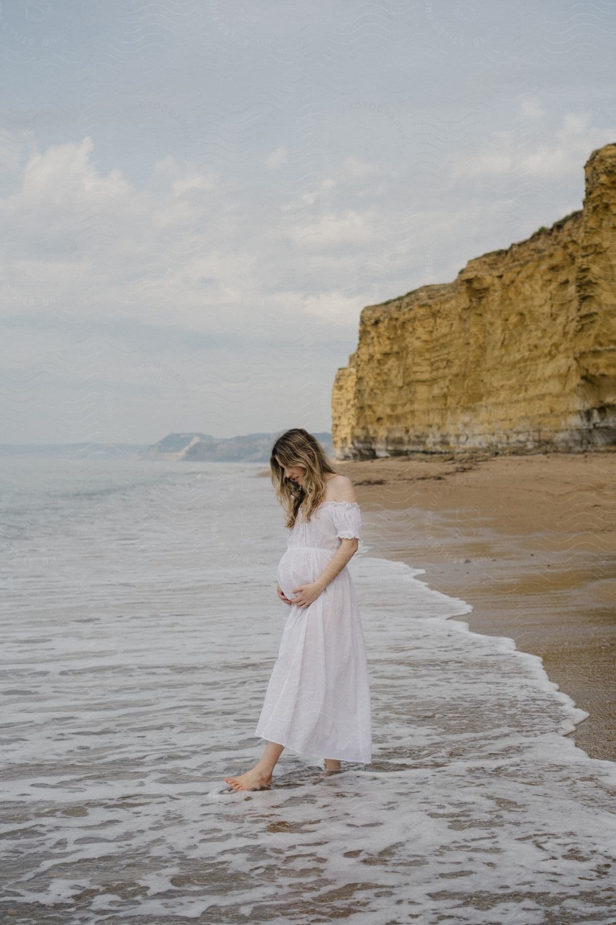 A woman is by the sea, near a cliff, looking at the sea.