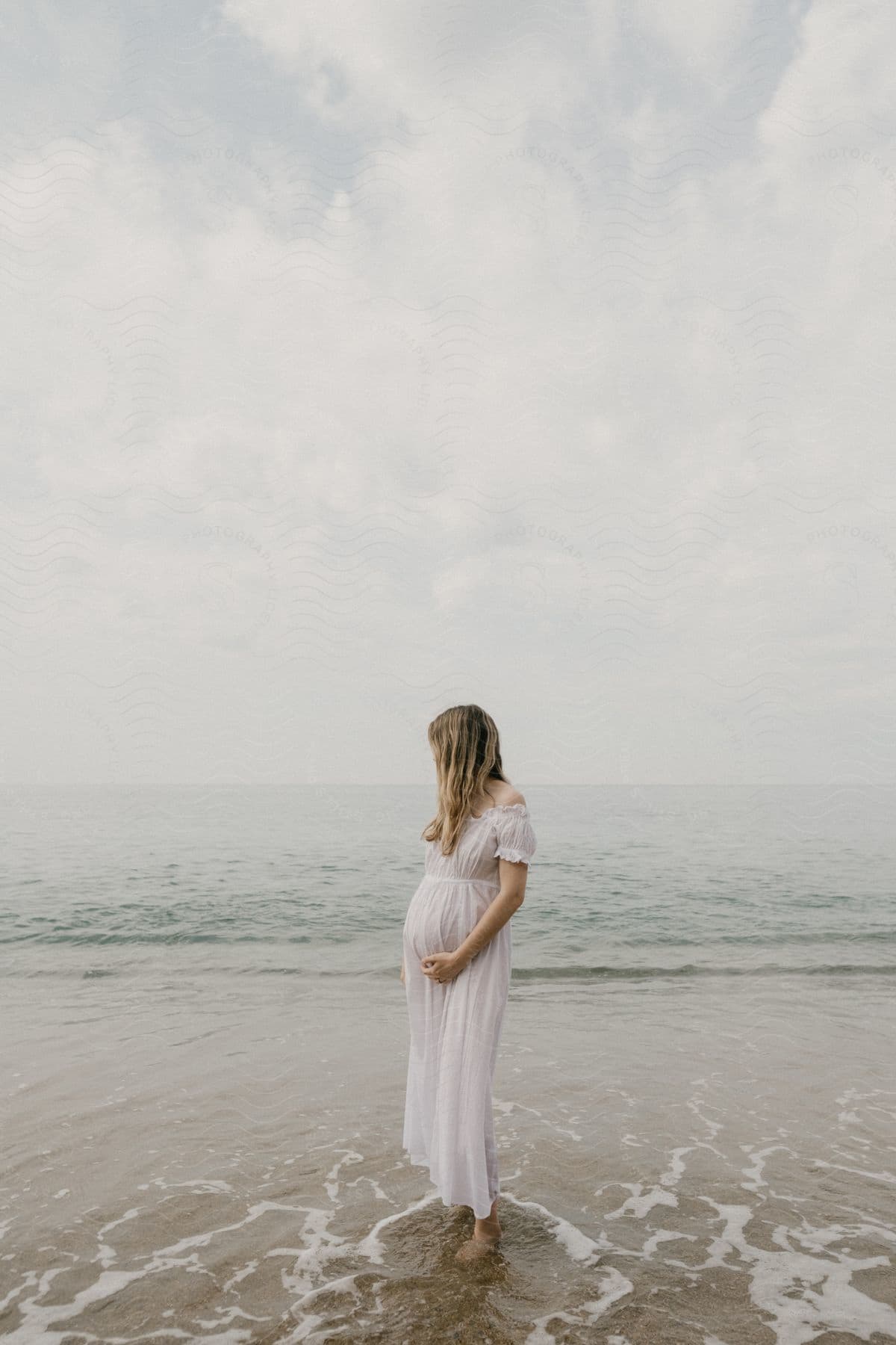 A woman standing on a beach holding her pregnant belly