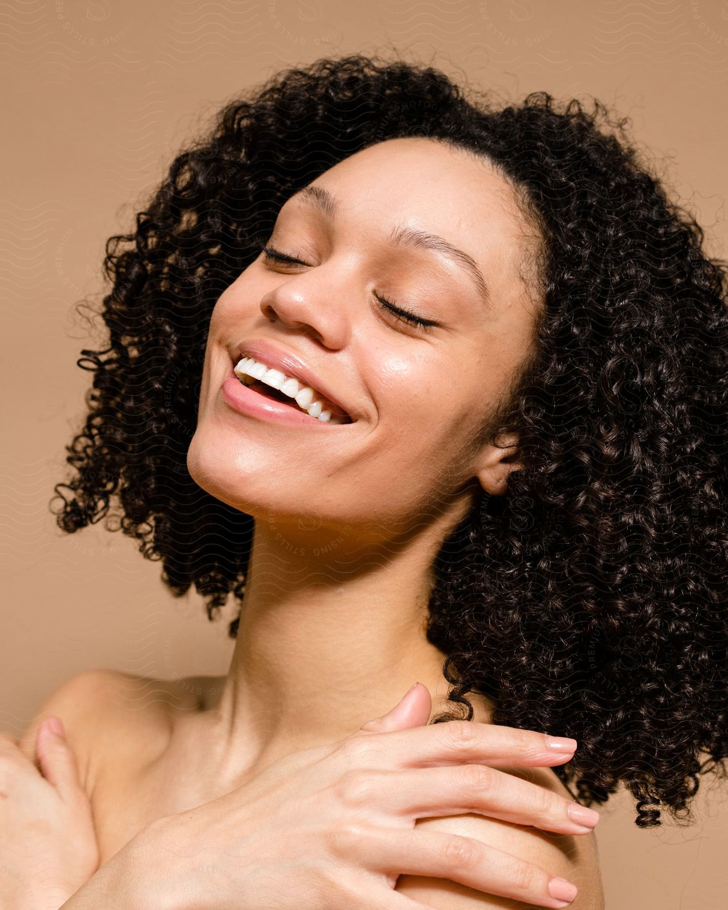 Woman smiling with her eyes closed and hands on her bare shoulders