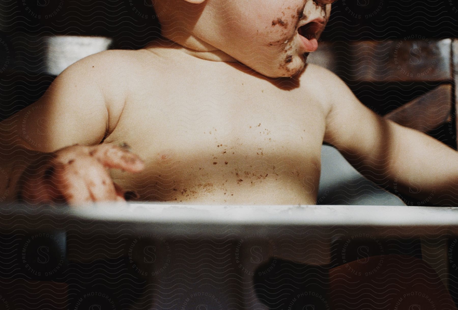 Baby with a dirty face sits in a high chair with their mouth open