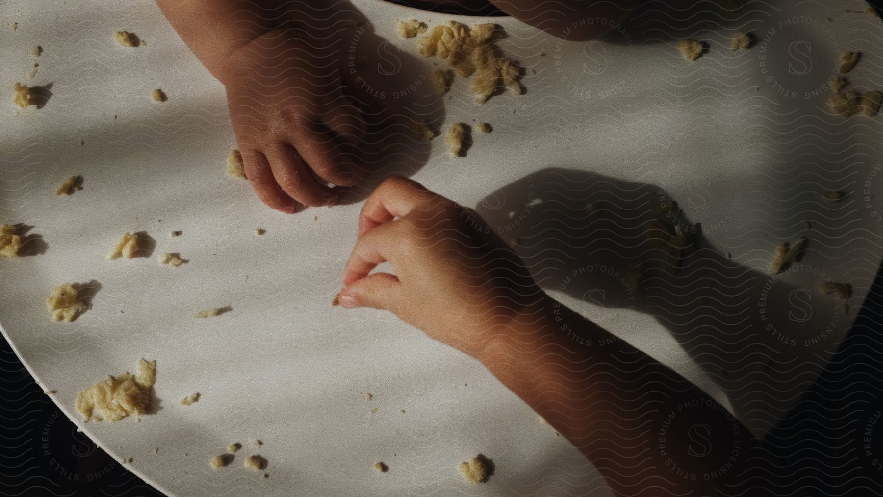 Two toddlers hands on a white table picking up scattered omelet.