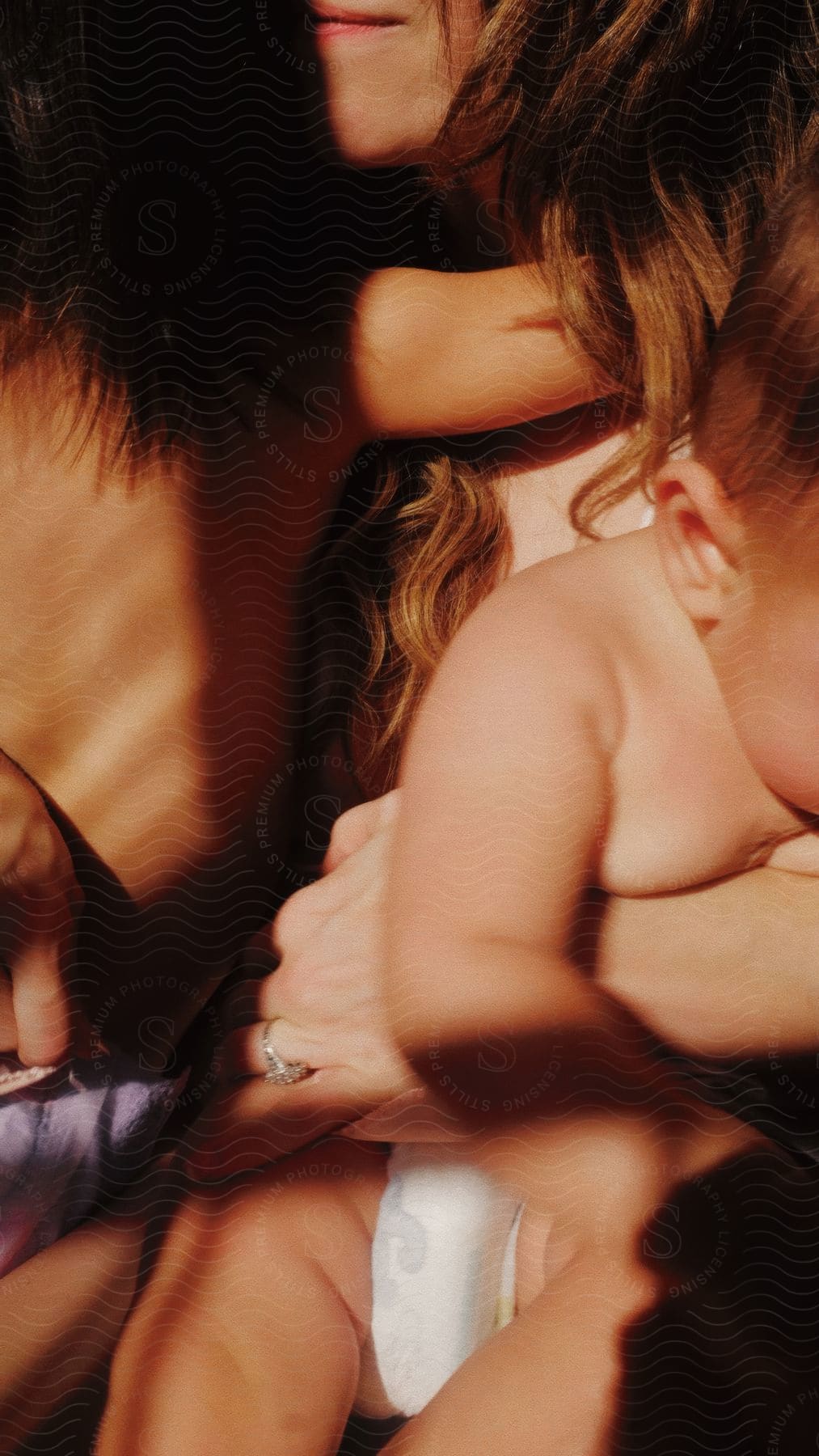 Mother holding her baby and hugging her young daughter, in a moment of affection, while they are being illuminated by soft sunlight.