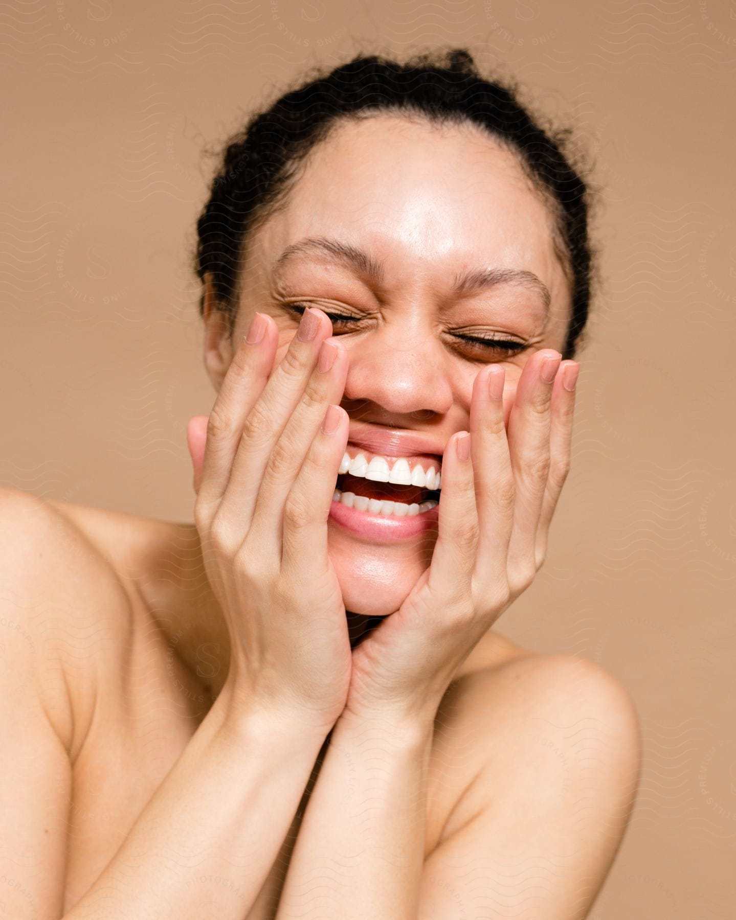 Portrait Of A Woman Without Her Shirt And With Both Hands On Her Face, Smiling And A Blurred Skin Tone Background