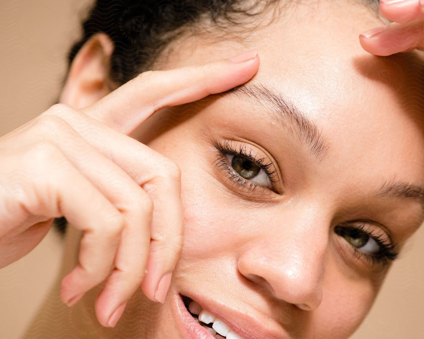 A woman smiles while framing her eyes with her fingers