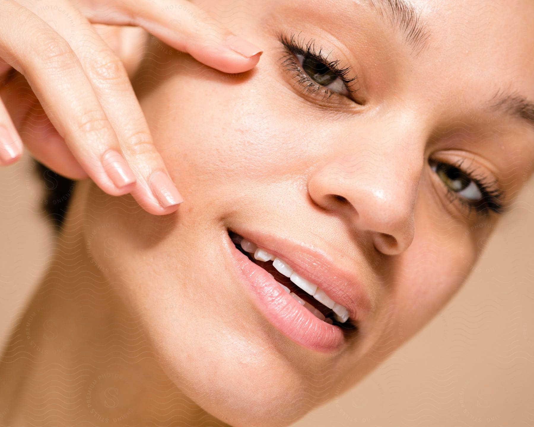 Portrait of a young woman with a slight smile with her black eyelashes highlighted and one of her hands on her face