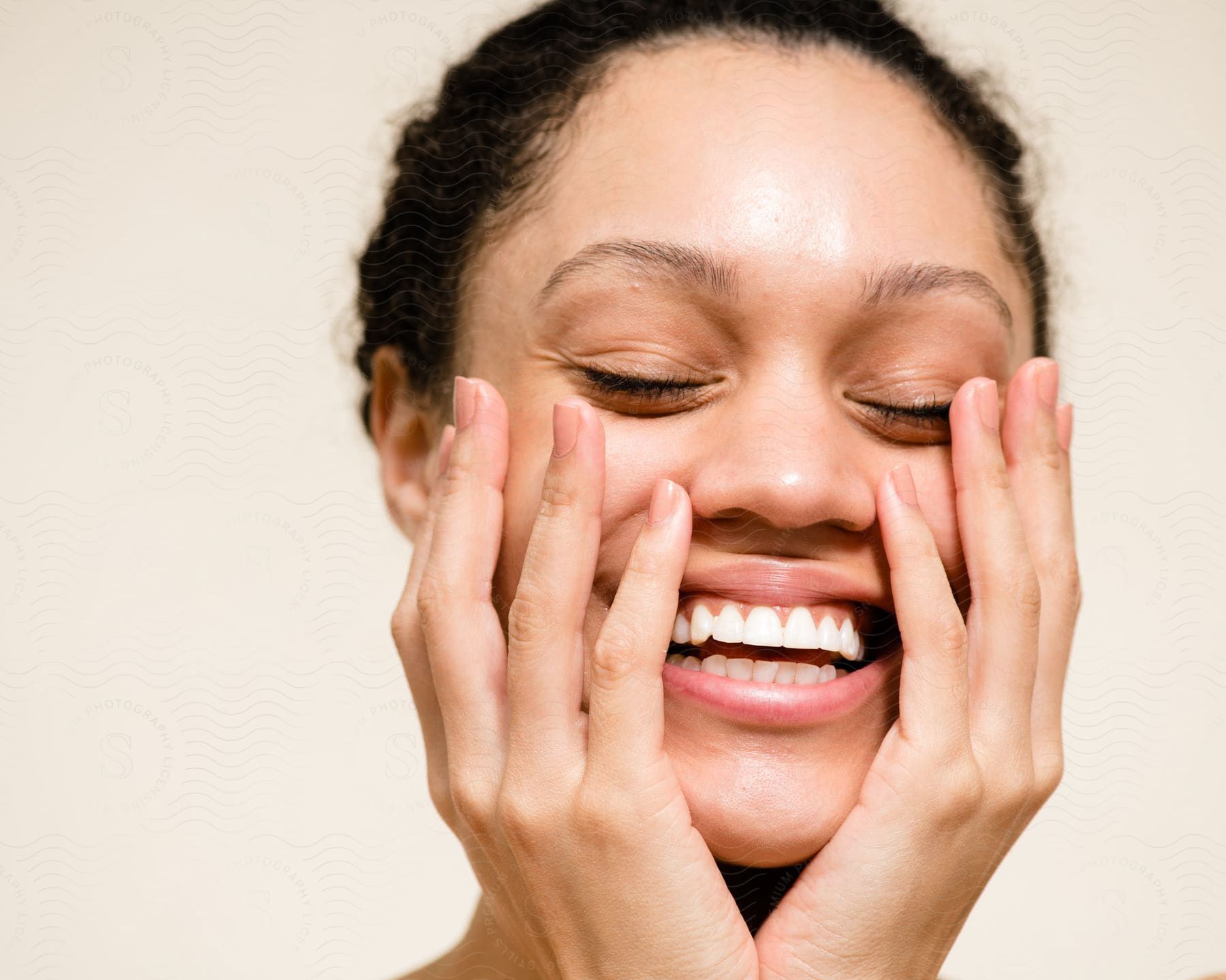 Portrait of a smiling young woman with black hair and with her two hands on her face