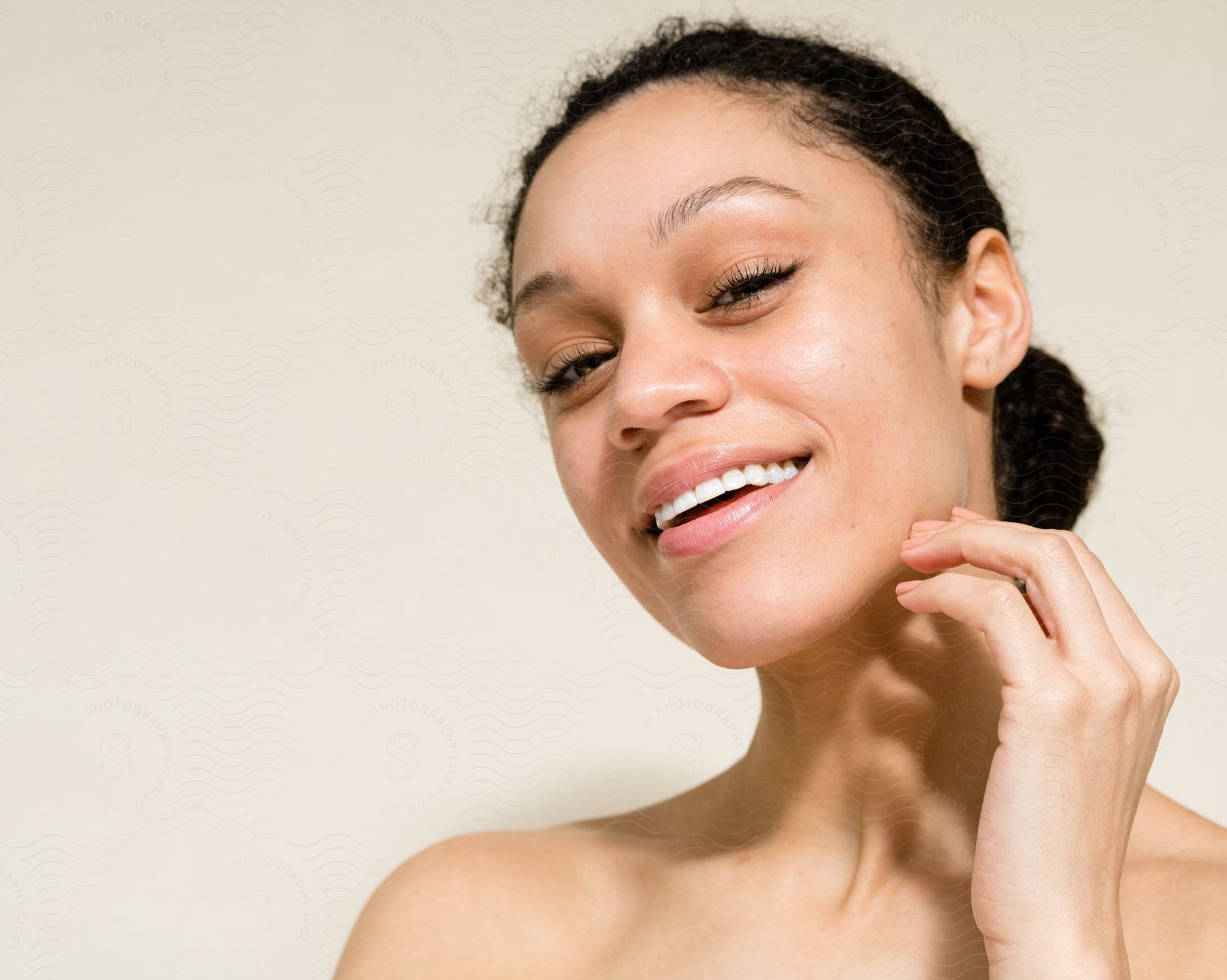 Smiling bare shouldered woman touches her jaw.