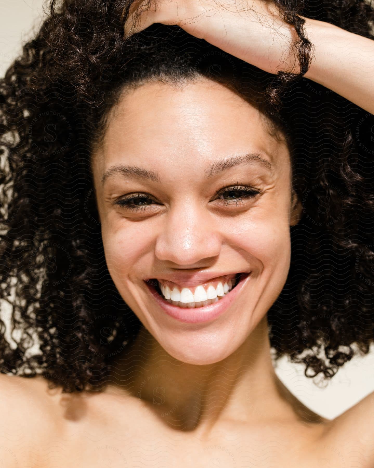 Woman smiles as she holds her hair up on her head with her hand