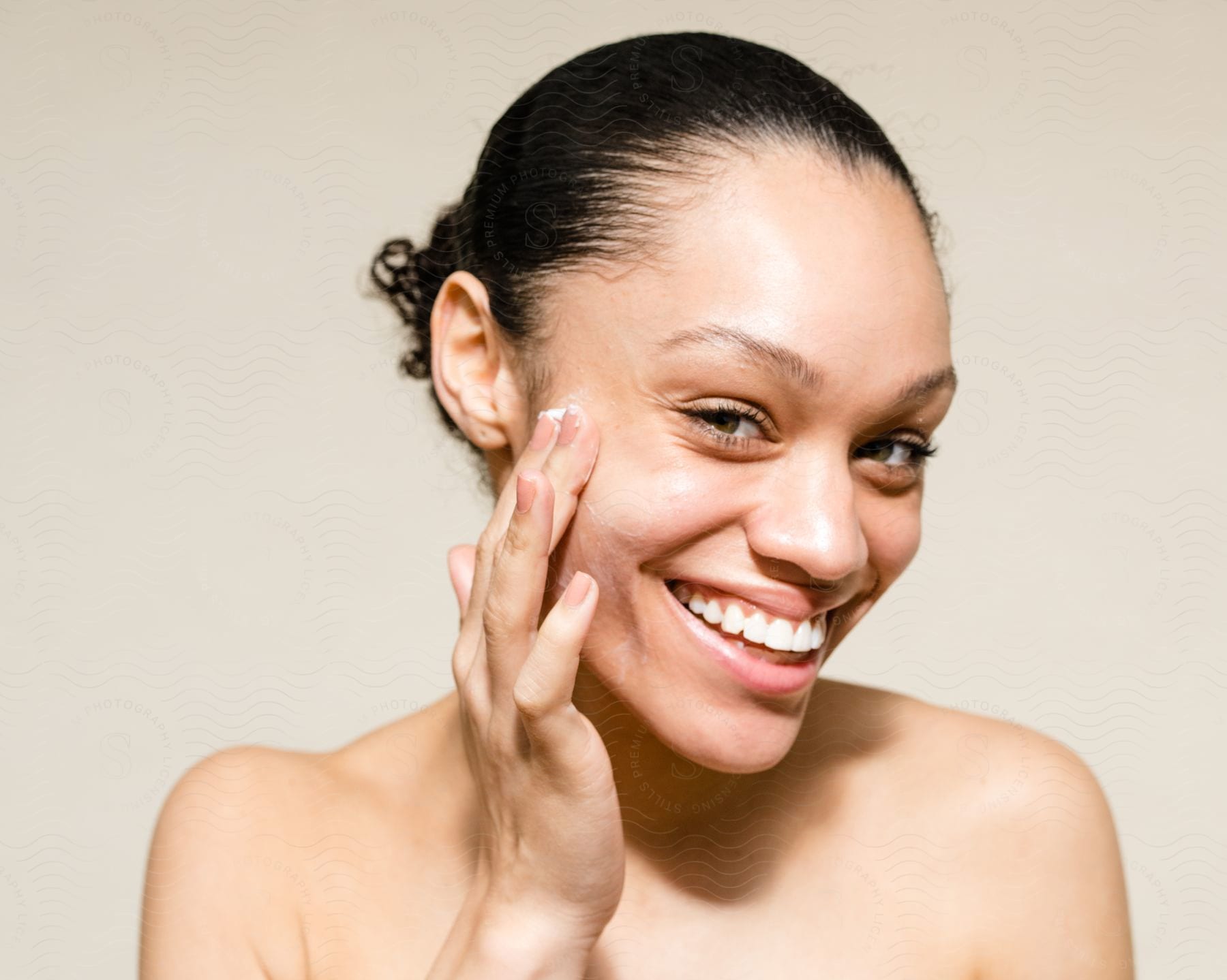 Close up of a female model applying cream to her face while looking at the camera