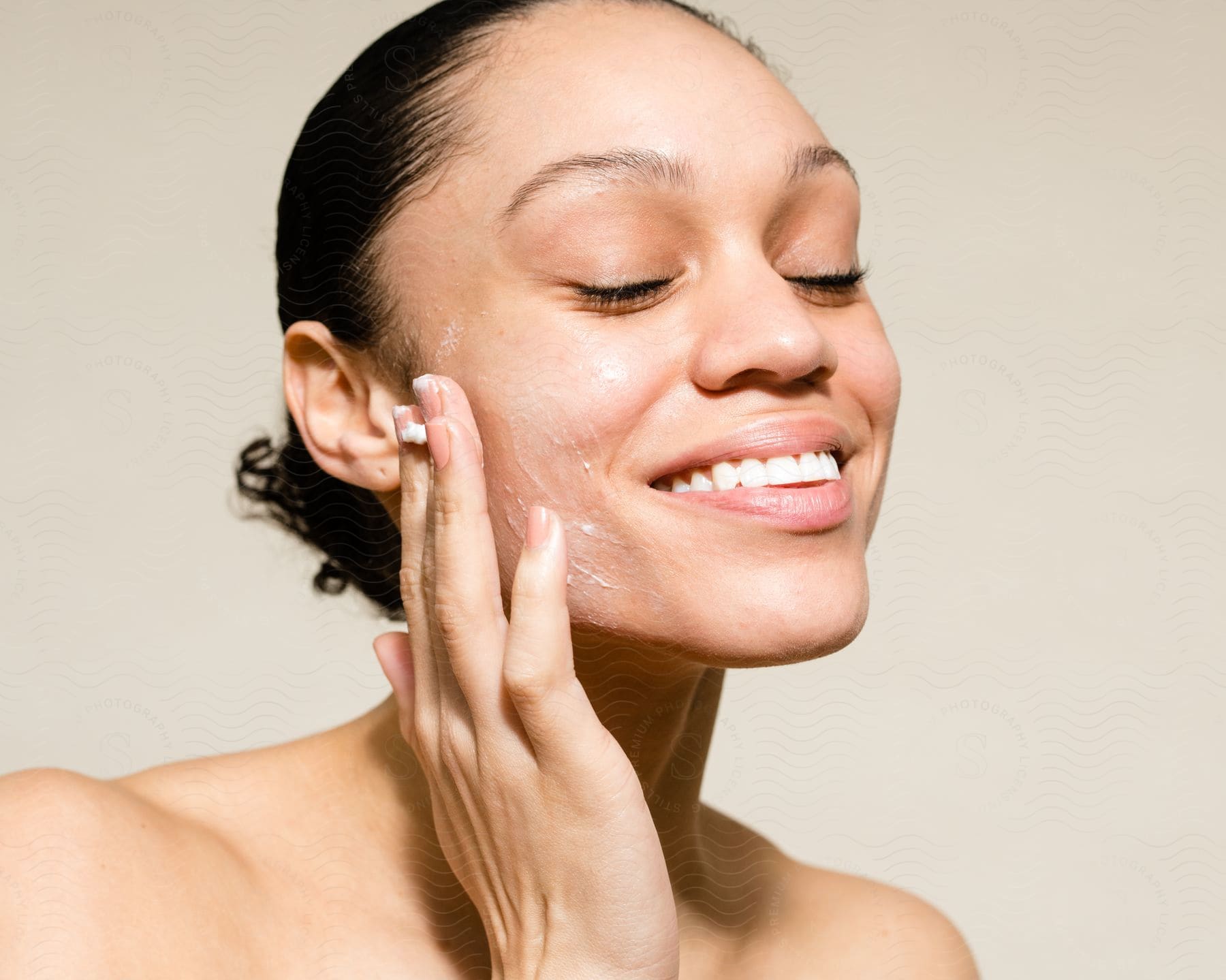 A woman smiling while spreading cream on her cheek
