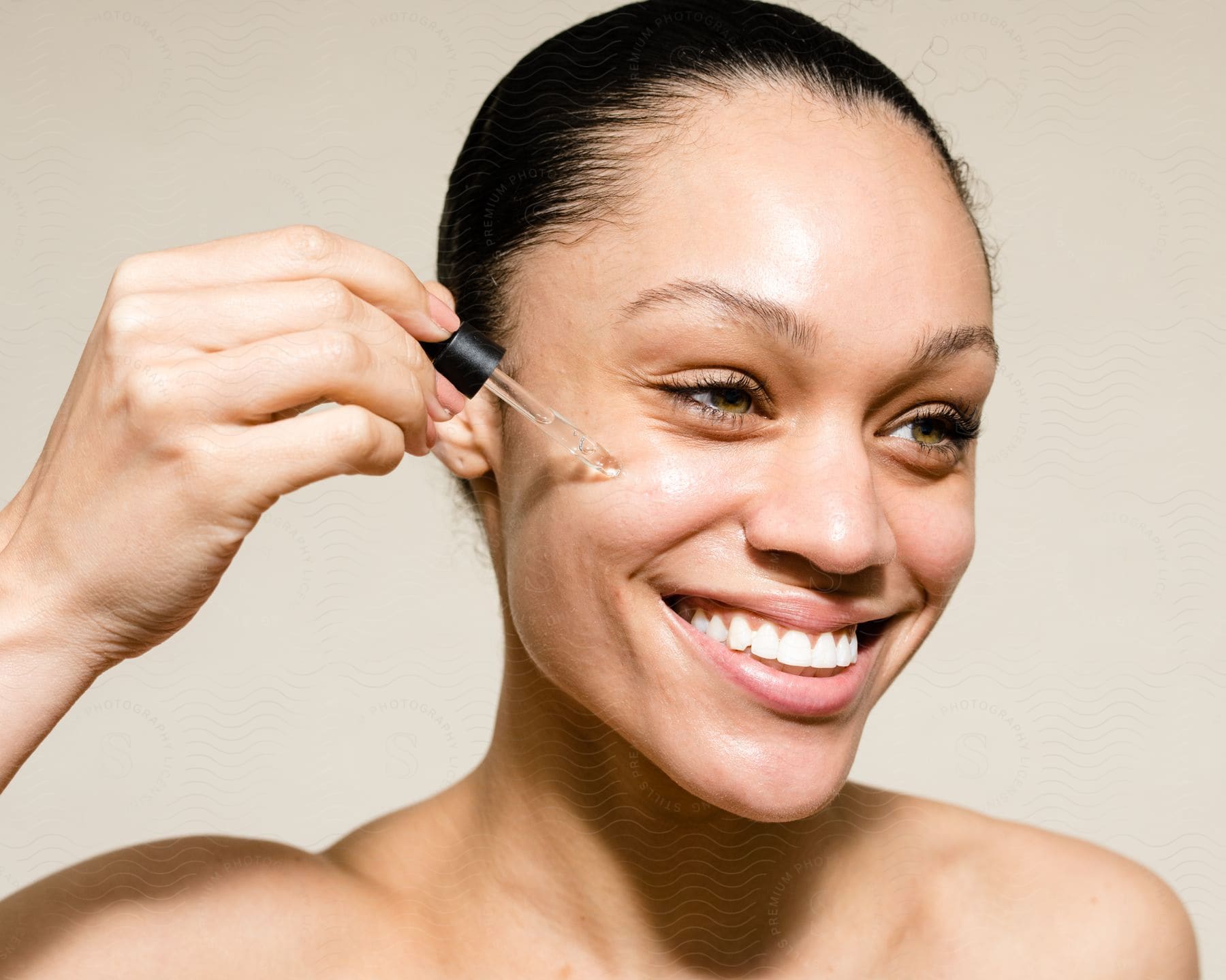 Smiling woman with tied black hair applying liquid serum to her face