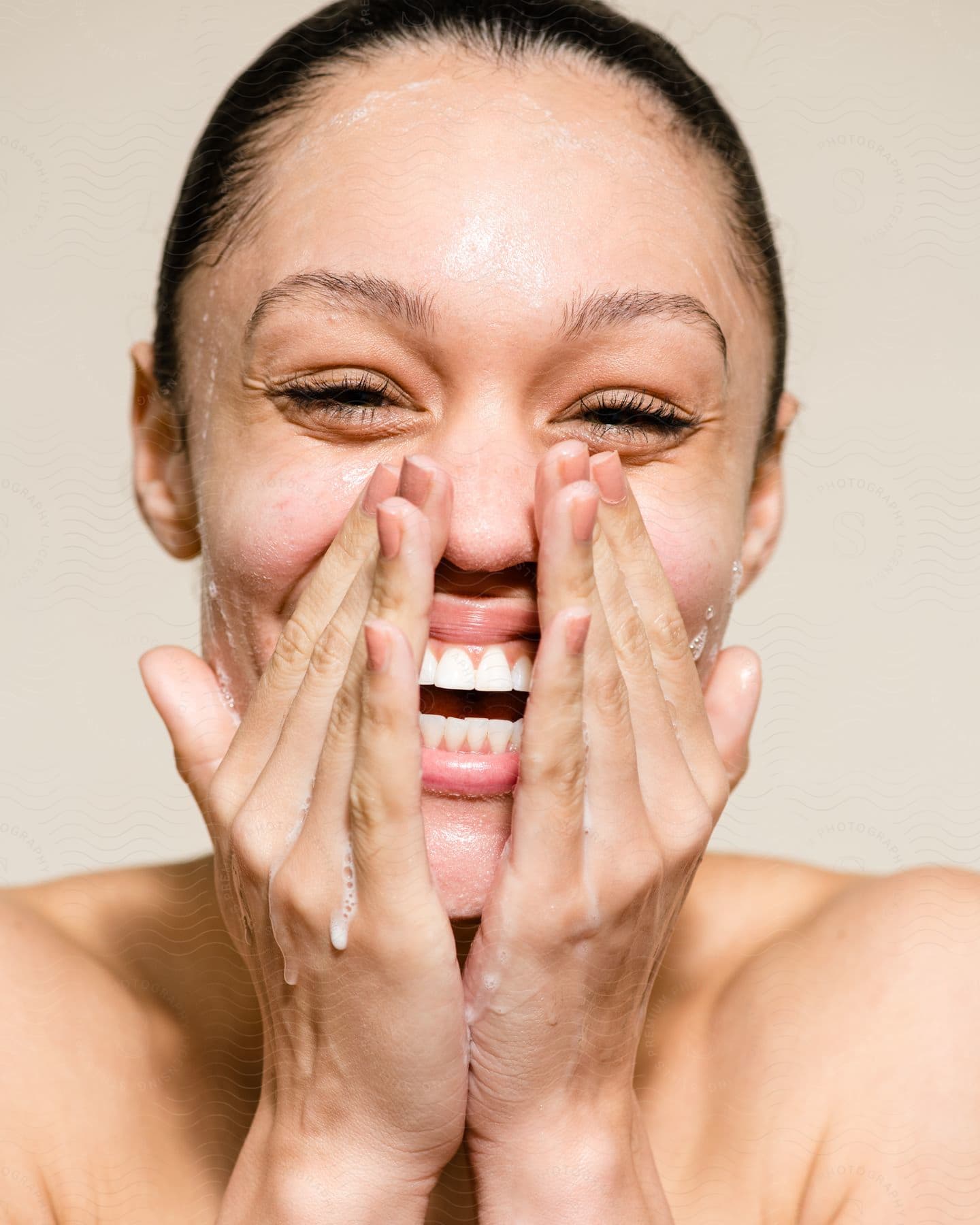 Portrait of a smiling young woman washing her face with soap and water running down her hands