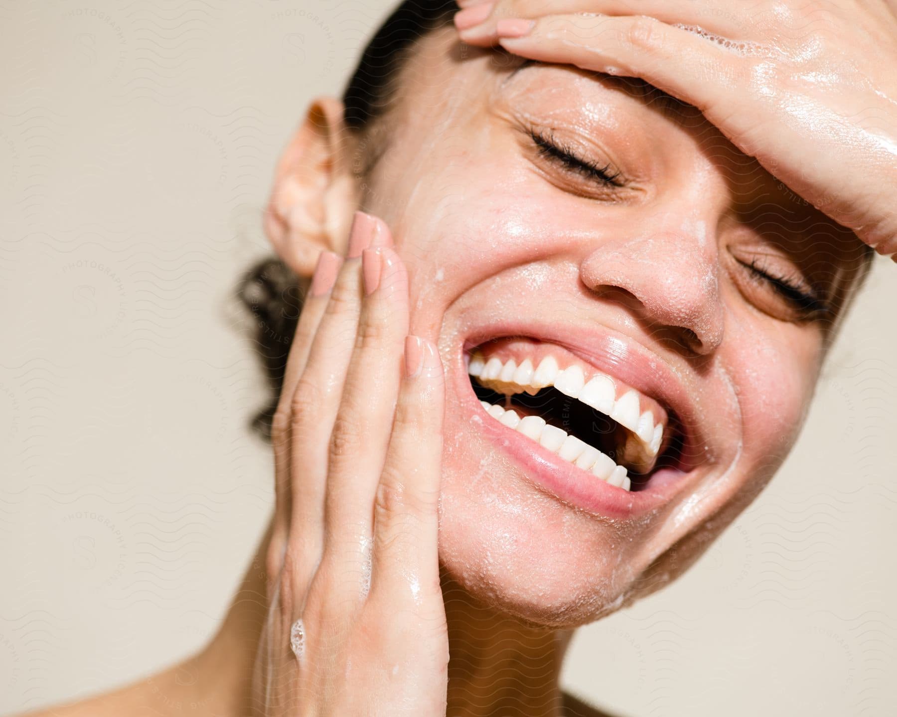 Close-up of a young woman laughing while cleansing her face.