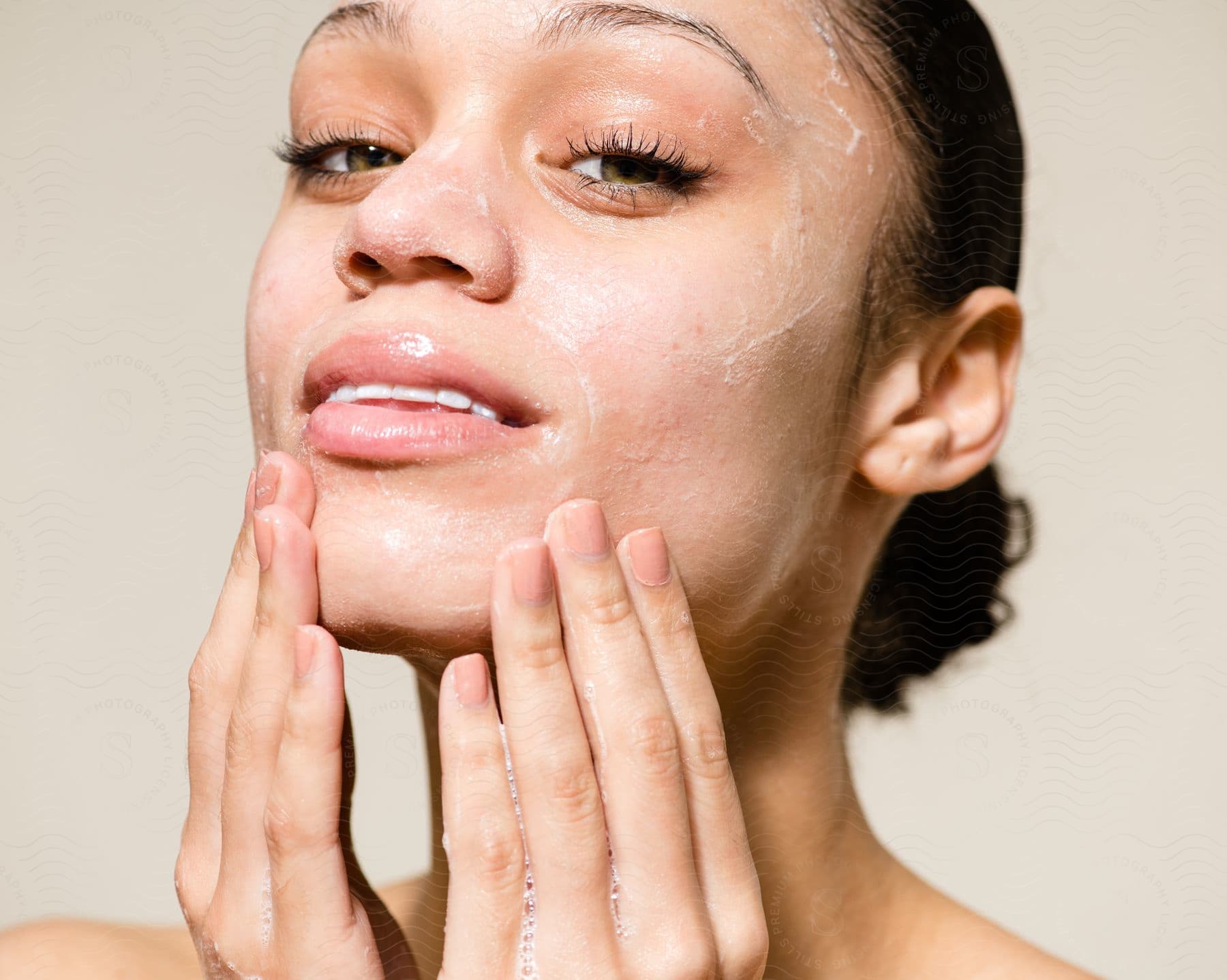 Woman touches lathered up face with both hands.