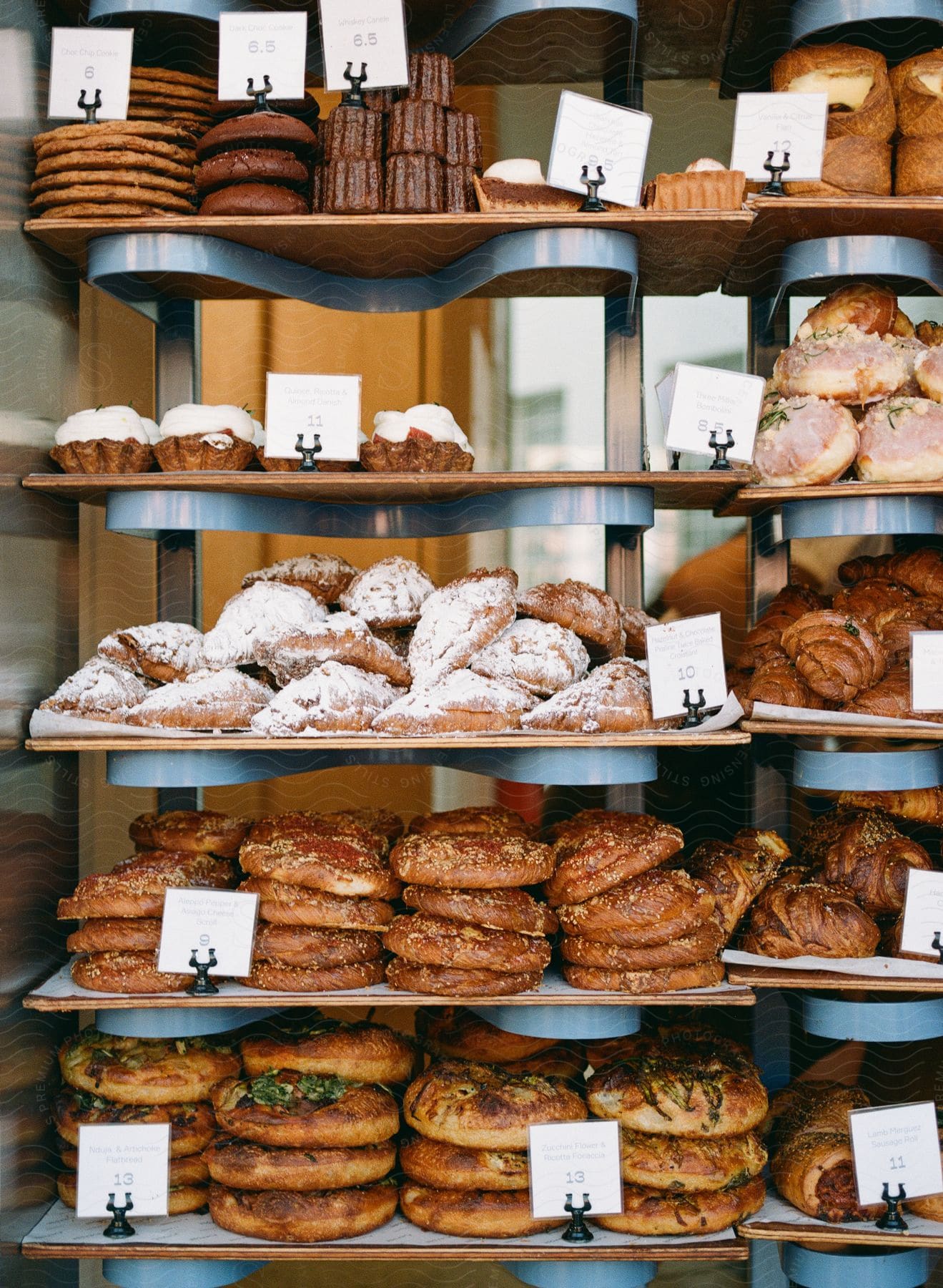 A bakery shelf filled with various pastries, including muffins and croissants, with name tags.