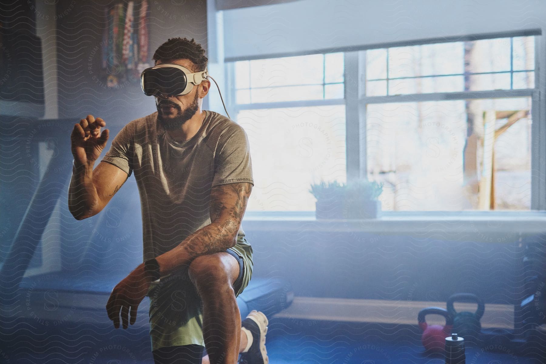 A man with tattoos, wearing VR goggles, appears to be interacting with a virtual environment in a gym setting.