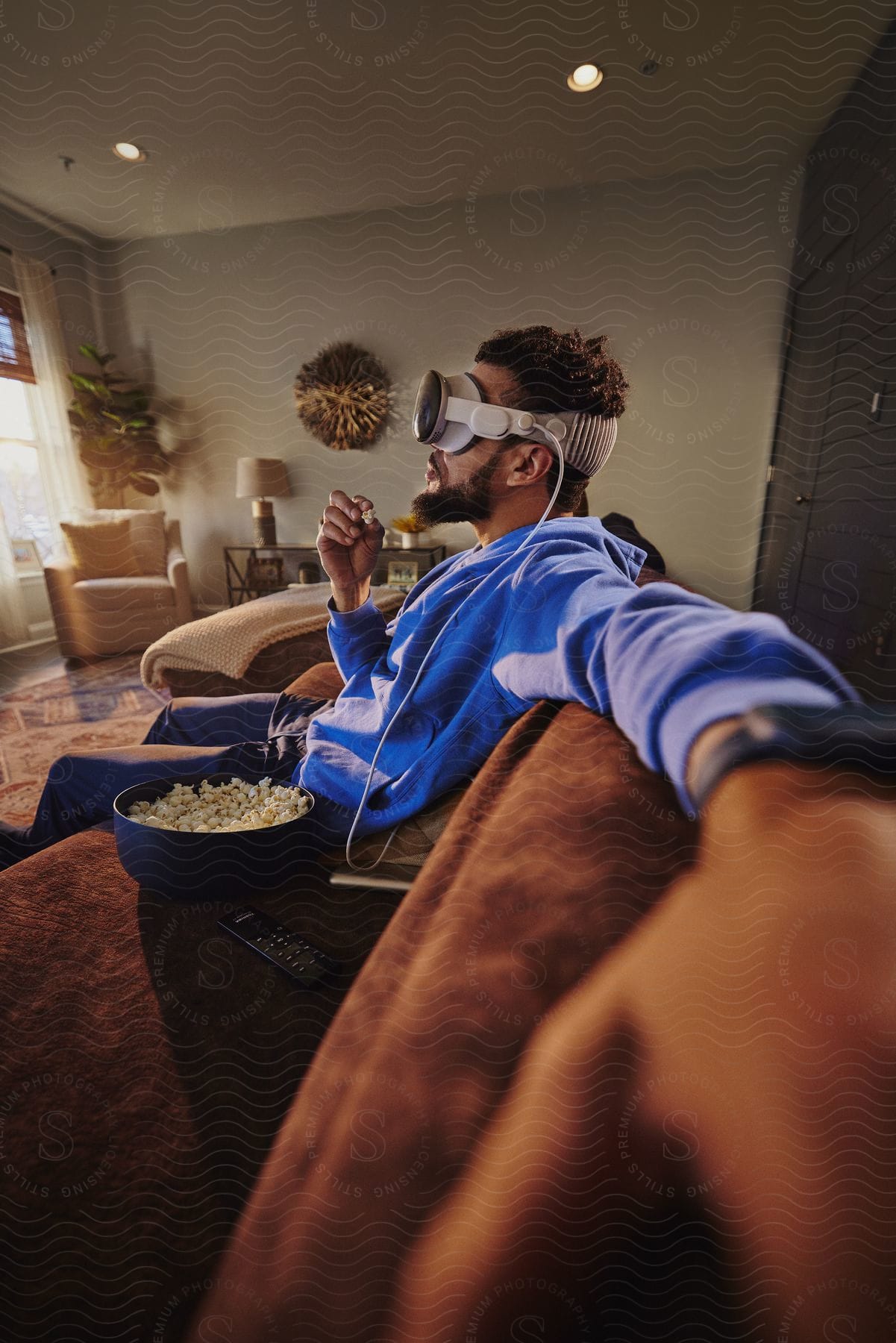 Man sitting on the couch with a bucket of popcorn next to him using virtual reality glasses