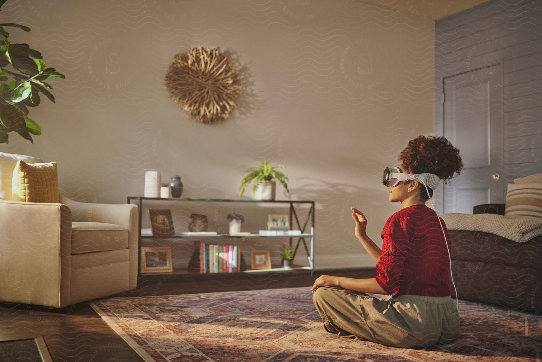 Stock photo of woman with vr headset sitting cross-legged on the floor, gesturing with hand in a living room.