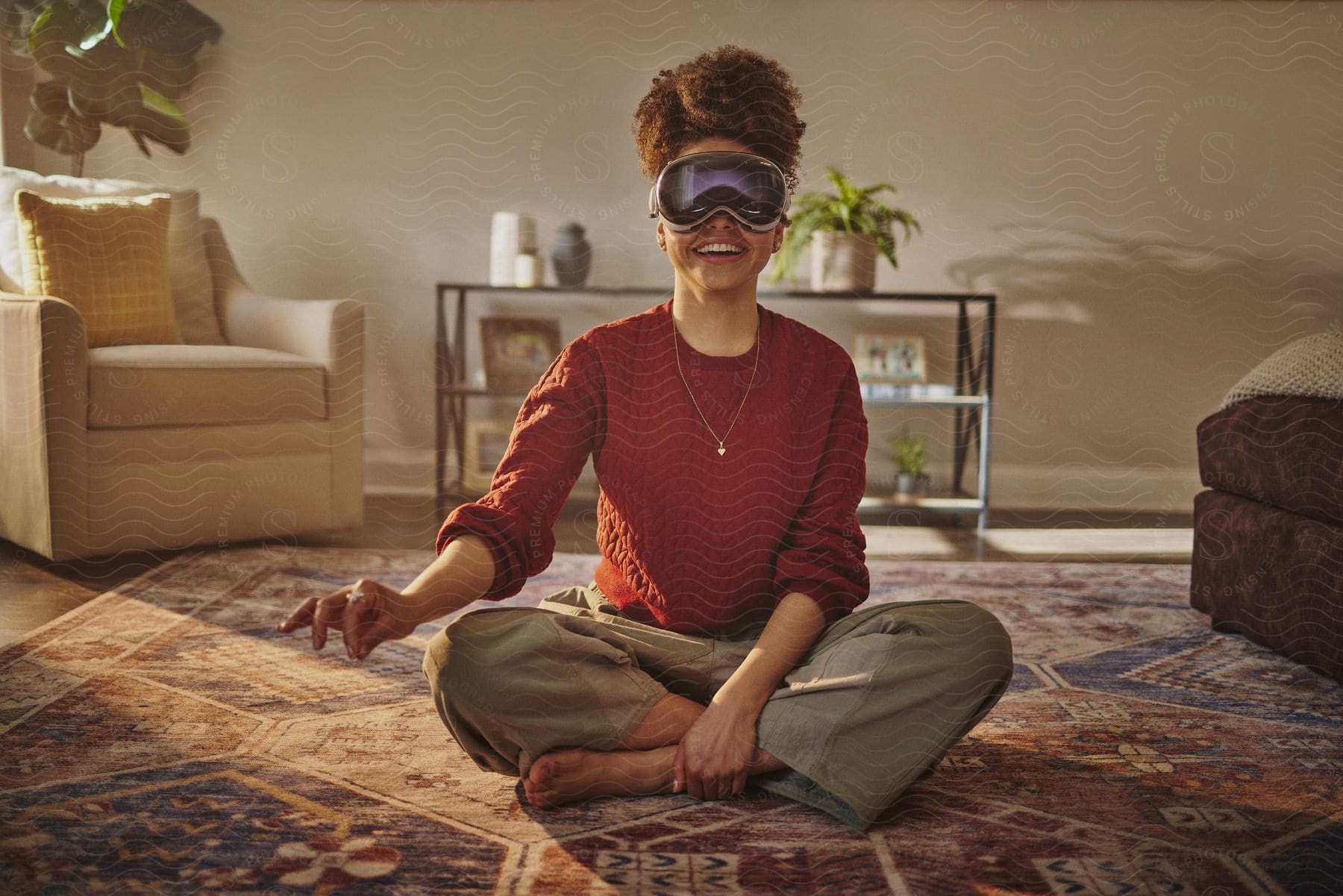 A woman is sitting on a rug in a living room and is smiling while wearing virtual reality glasses and has one hand pointing forward