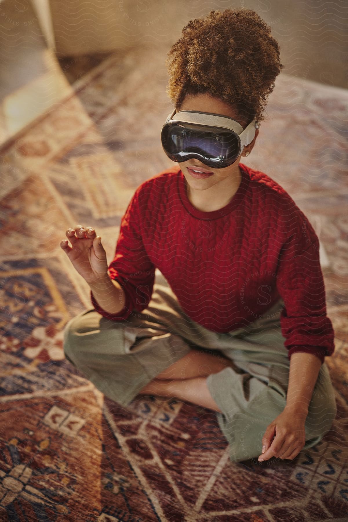 Young woman sitting on carpet with one hand raised using virtual reality glasses